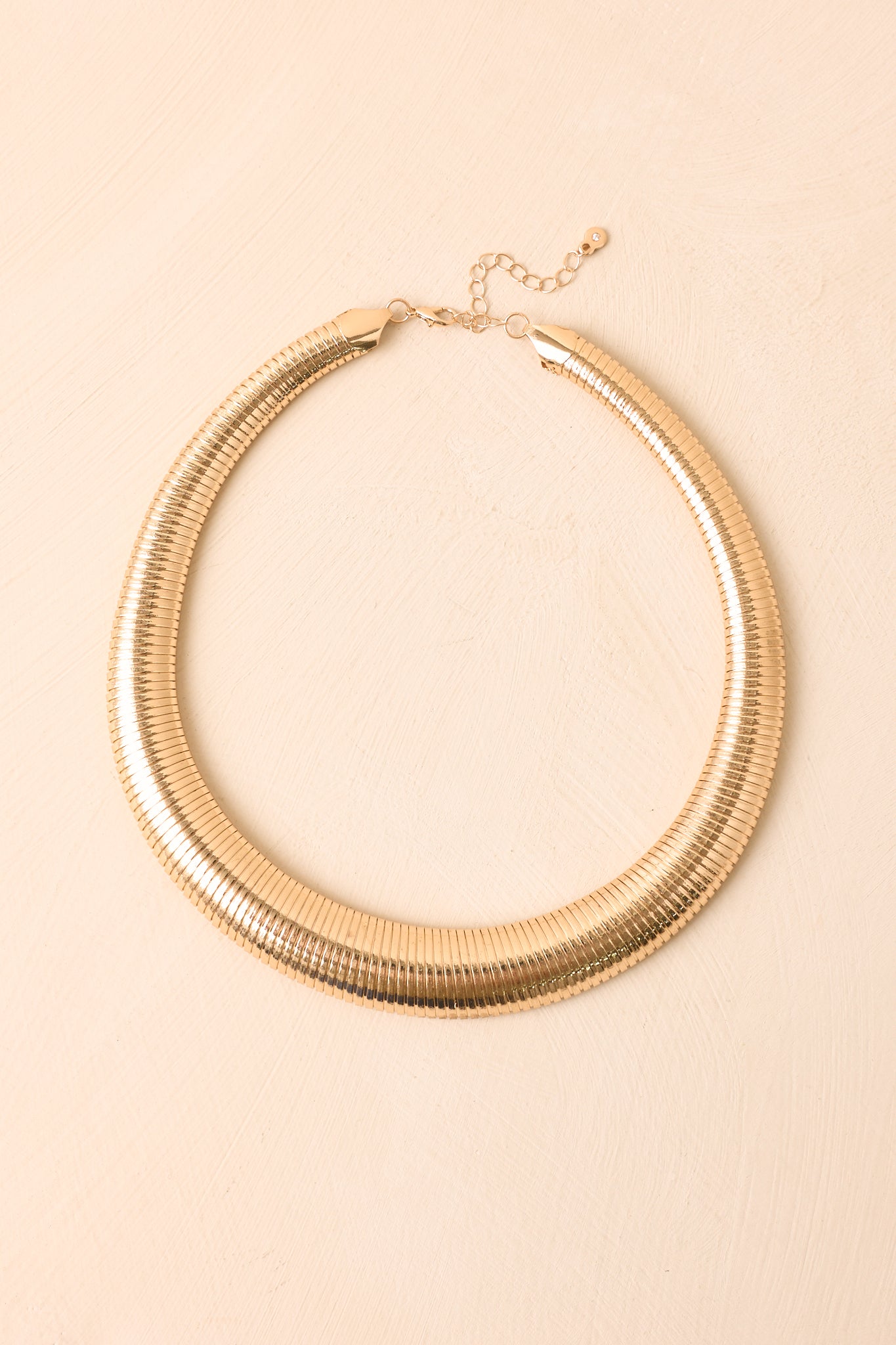 Gold-tone necklace displayed against a neutral background, highlighting the curved shape, graduated width, and sculptural silhouette.