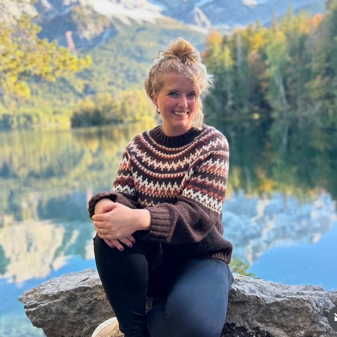 Woman sitting on a rock by a lake with mountains in the background.