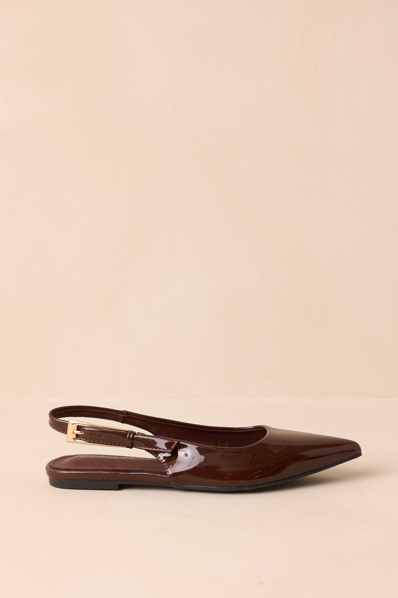 Side view of dark brown patent flats on a beige background emphasizing the slingback strap and flat sole.