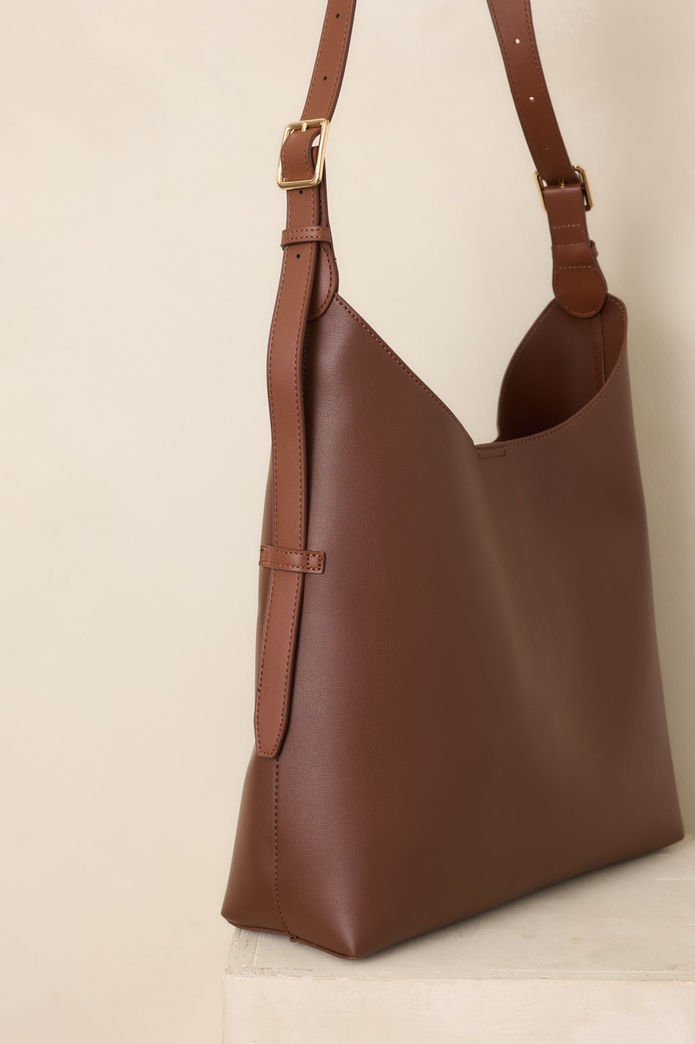 Close-up of the dark brown handbag's magnetic tab closure and smooth finish, highlighting its refined minimalist design.