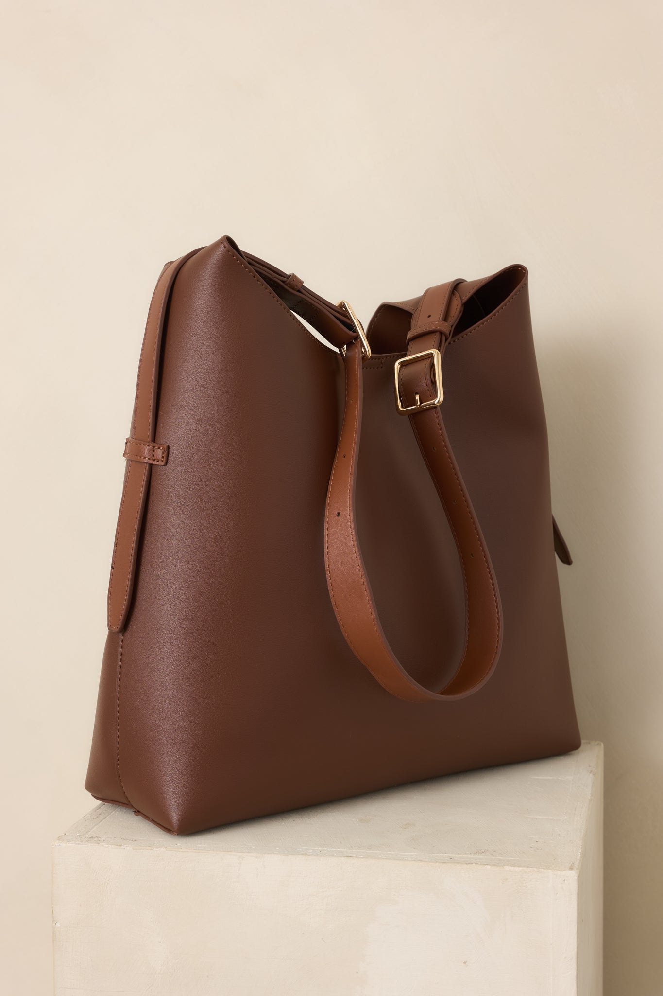 Dark brown carryall handbag with a minimalist silhouette, adjustable shoulder strap, magnetic tab closure, spacious main compartment, and coordinating zip pouch.