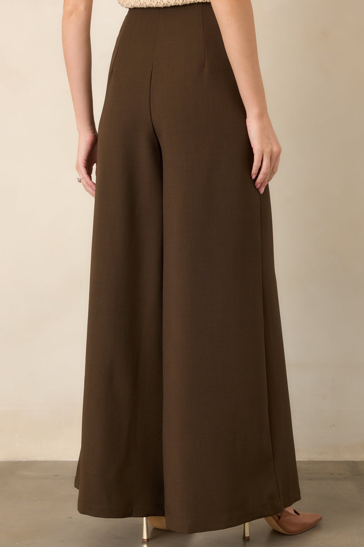 Rear view of the dark brown wide-leg pants showcasing the smooth woven fabric, high-rise waist, concealed back zipper, and tailored silhouette.