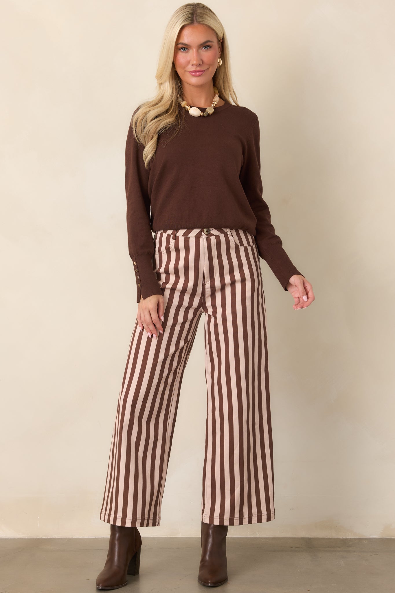 Dark chocolate long-sleeve top with a crew neckline, straight silhouette, ribbed trim, and elongated cuffs accented with gold-tone buttons.