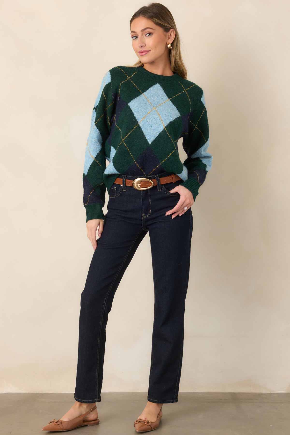 Soft knit sweater with a dark green base, contrasting blue diamond motifs, delicate golden lines, and an easy crew-neck silhouette.