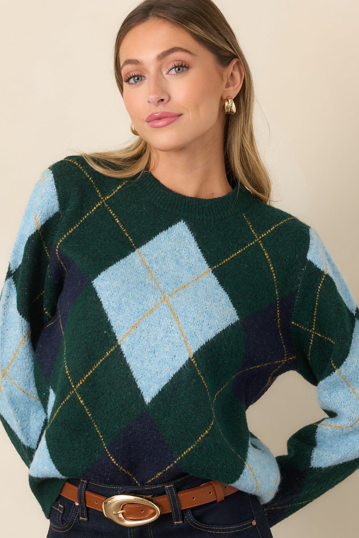 Close view of the diamond-patterned knit sweater highlighting the light blue and navy motifs against the dark green base.