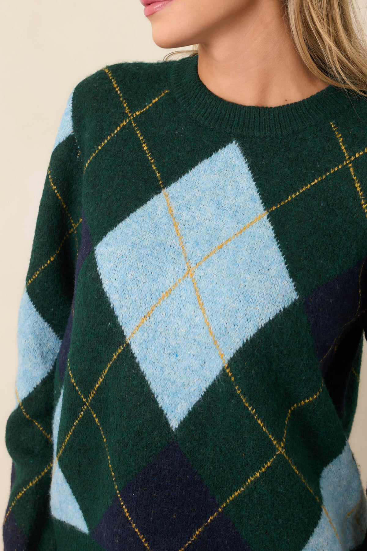 Detailed view of the sweater's geometric knit pattern, featuring blue diamond accents and fine golden yellow lines across the dark green base.