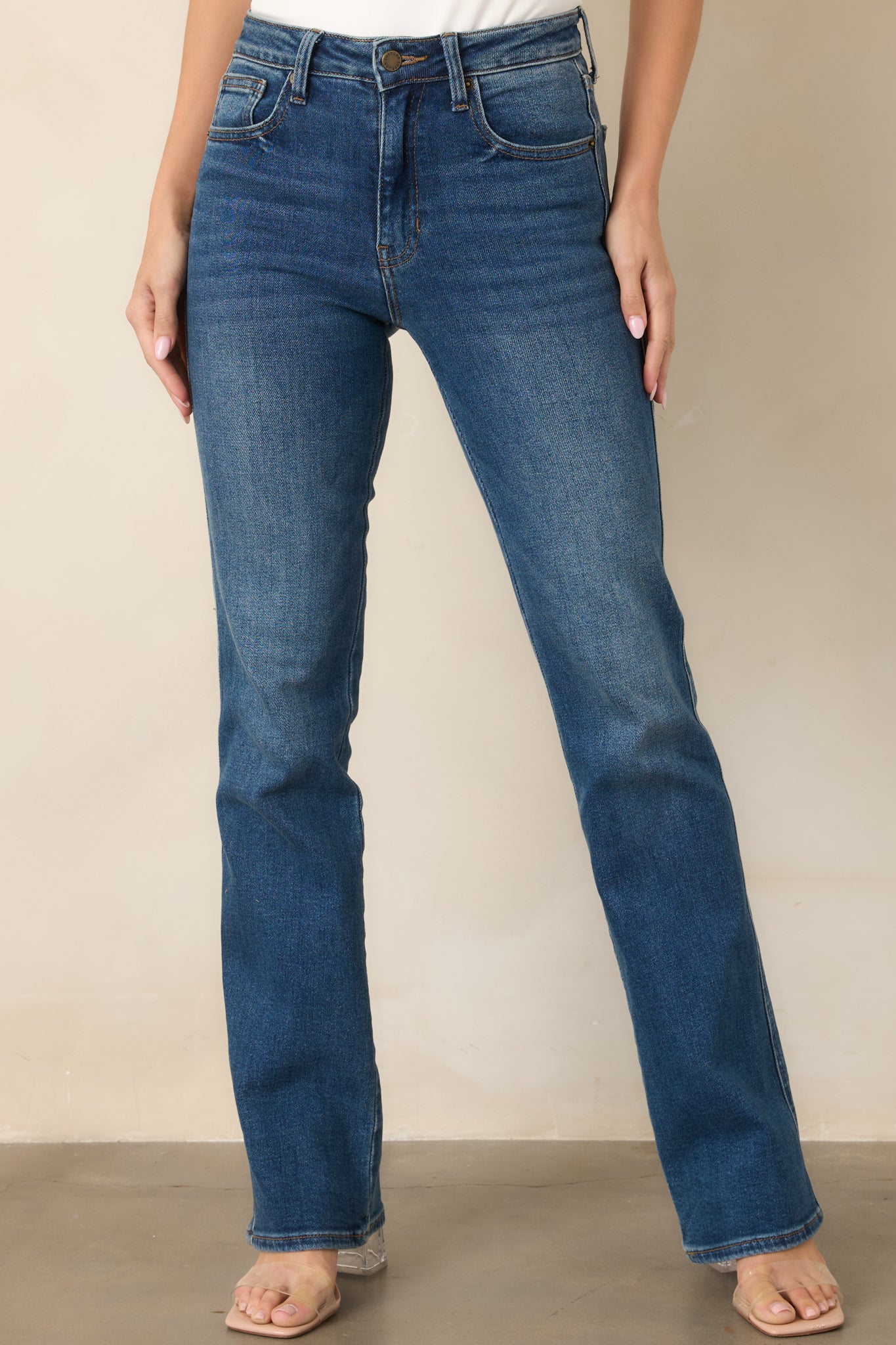 Close view of the dark indigo jeans highlighting the high-rise waist, belt loops, button closure, and subtle whiskering.