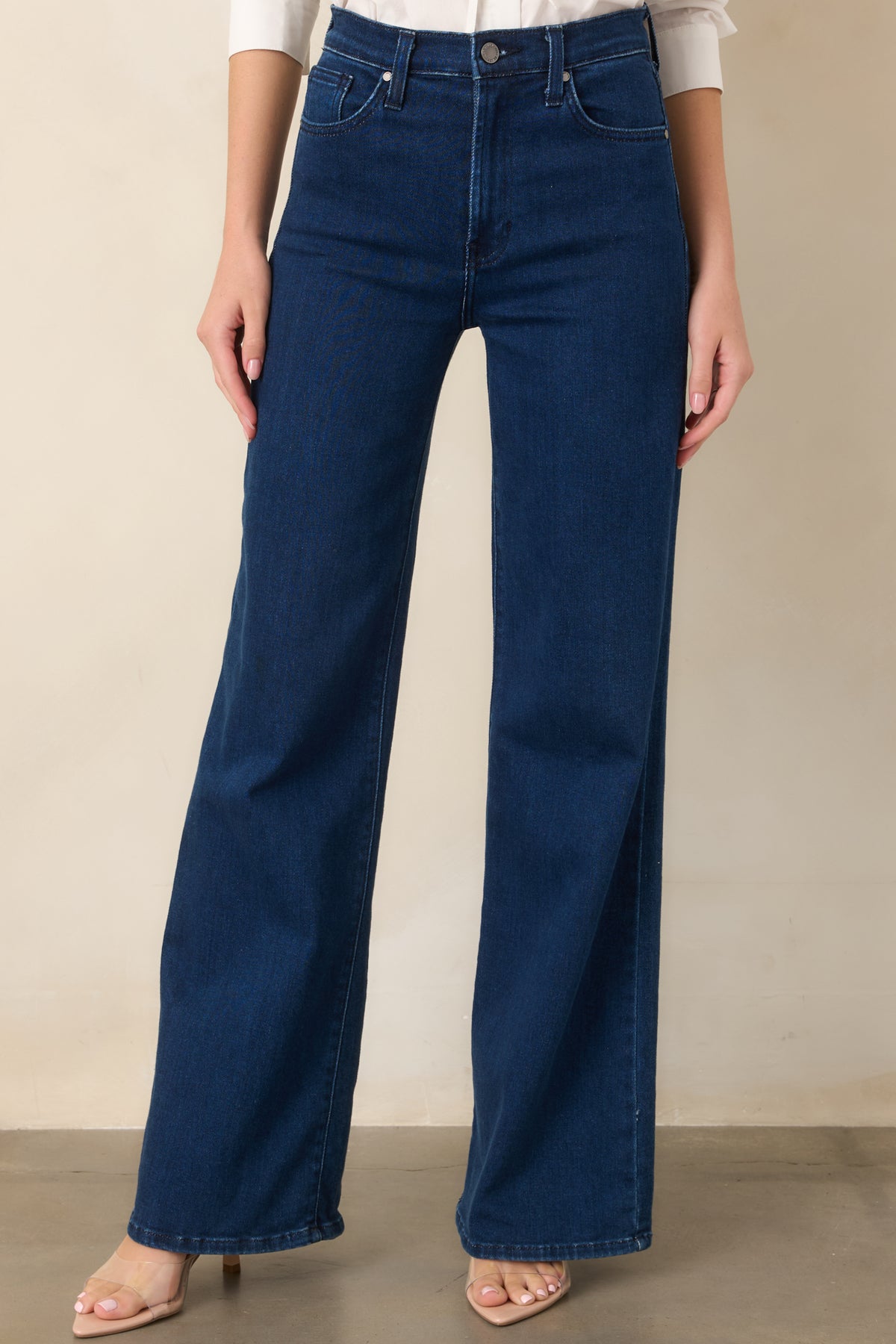 Upper portion of the dark jeans showing the elevated waistband, belt loops, front pockets, and neatly concealed zipper fly.