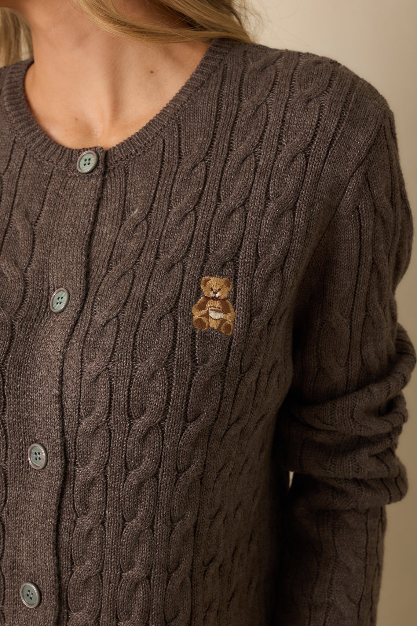 Tight detail of the dark mocha knit pattern with tonal button closure and fine embroidered teddy bear patch.