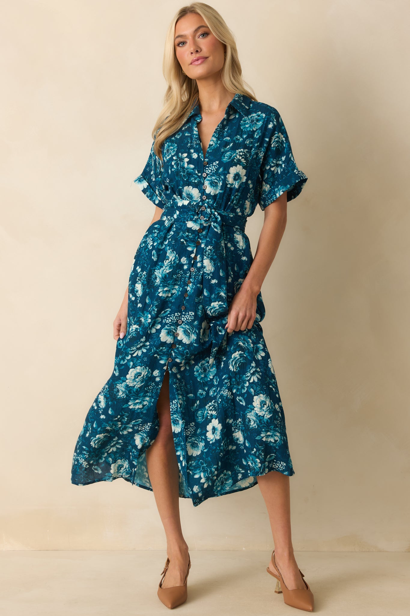 Short-sleeve dark teal dress with collared neckline, elasticized waist, and a flowing skirt adorned with multicolor flowers.