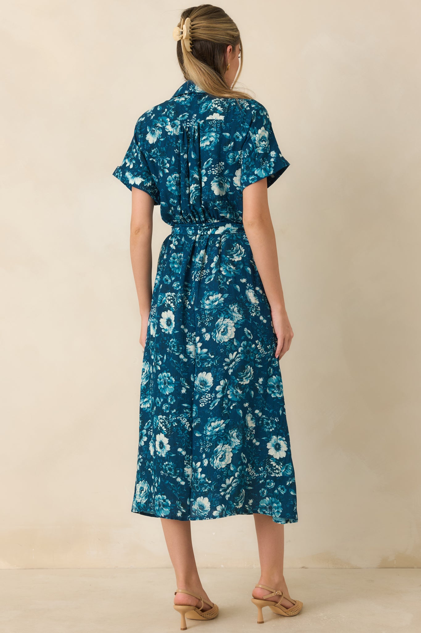 Back view of the dark teal floral dress showcasing the printed fabric, waistband, and short sleeves.

