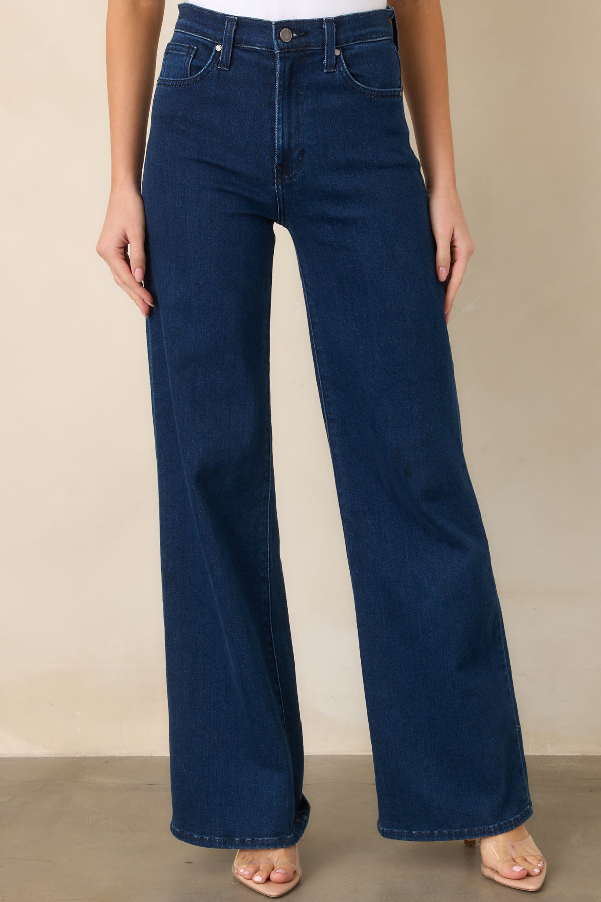 Dark wash denim highlighting the high-rise waist and zipper button closure.
