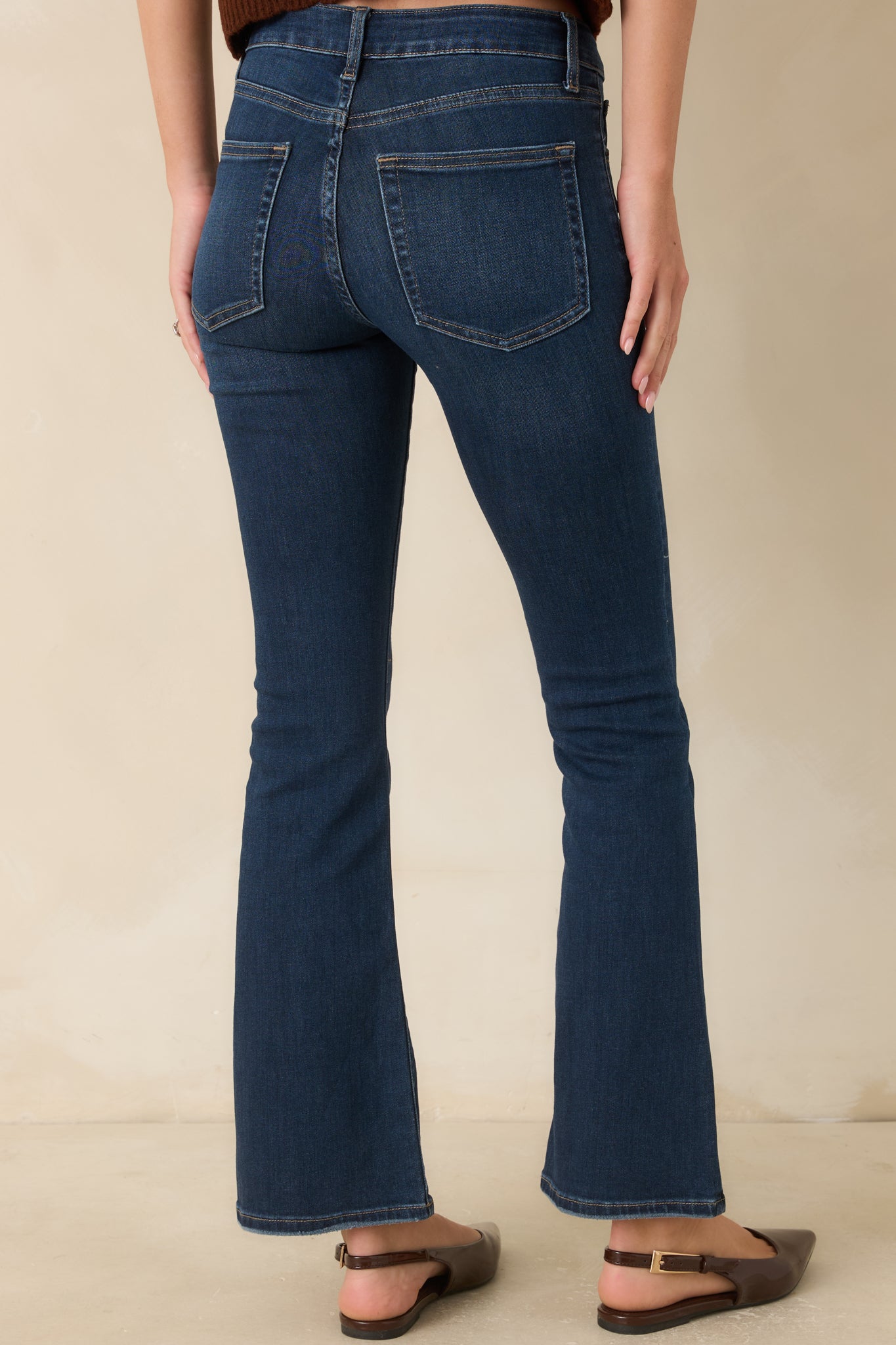 Rear view of dark wash mid-rise flare jeans with classic back pockets, contrast stitching, and a fitted silhouette that opens into a subtle flare.