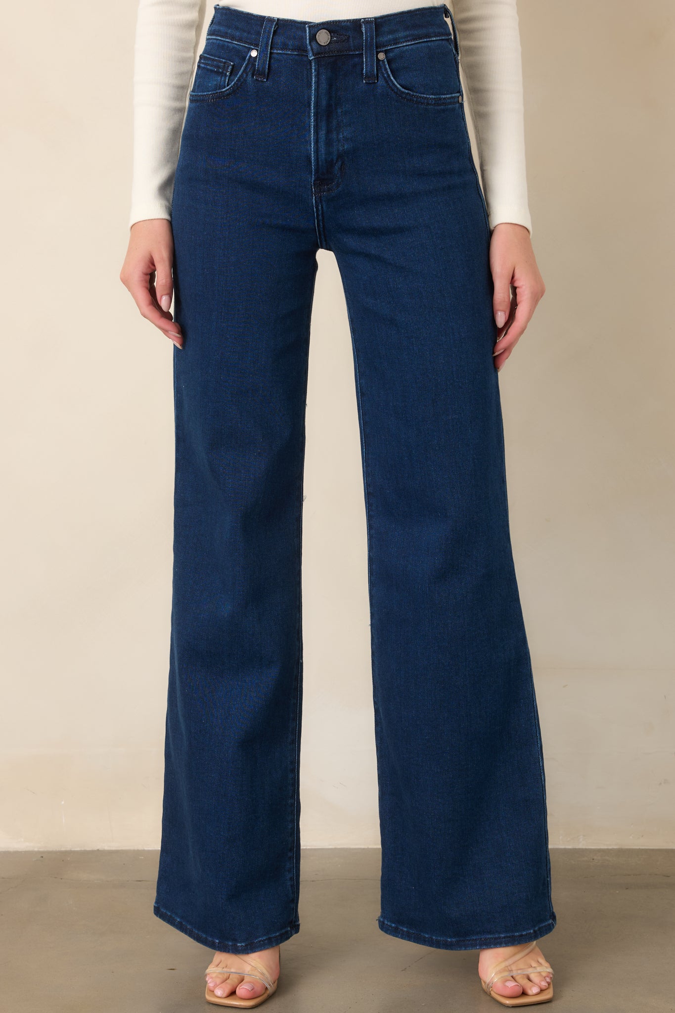 Close view of the dark wash jeans highlighting the high-rise waistband, button and zipper closure, and front pocket construction.