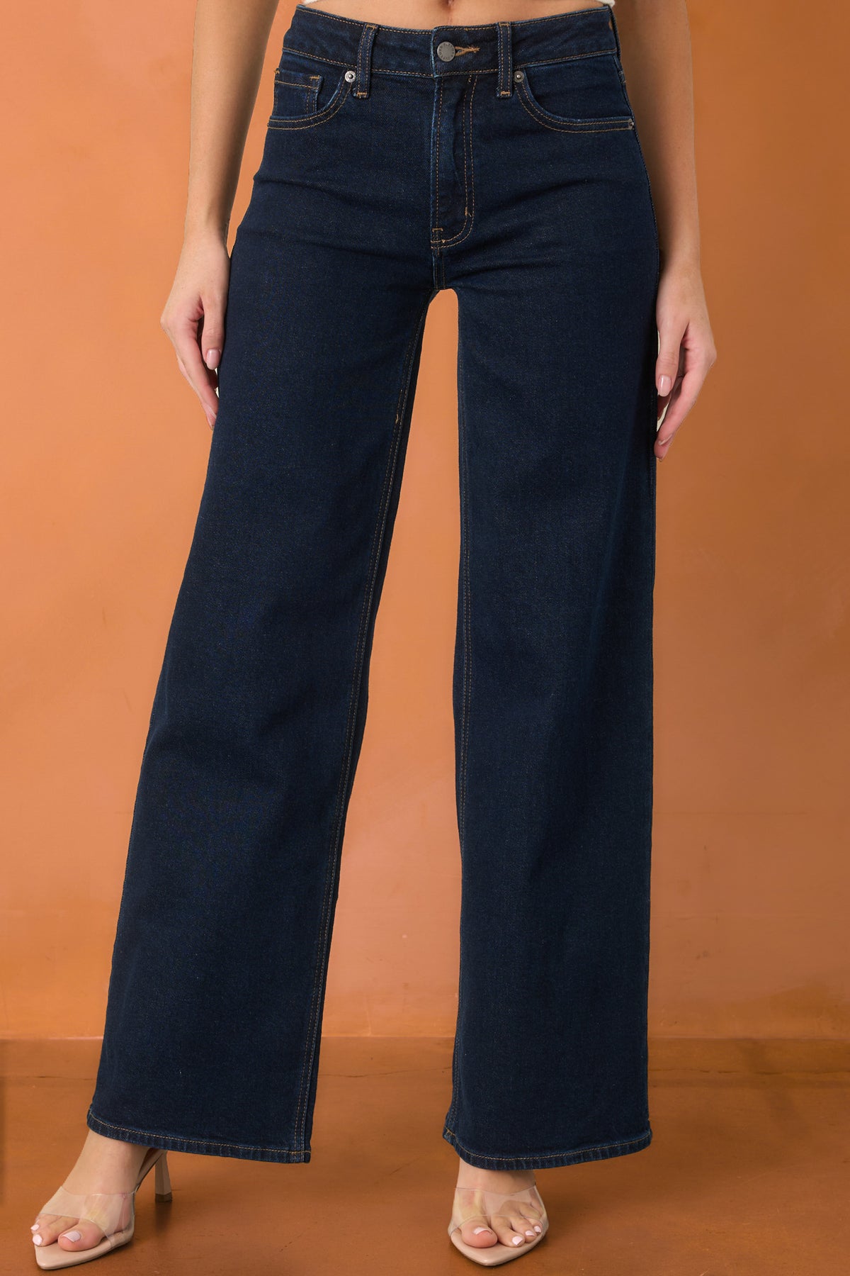 Close view of the dark wash jeans highlighting the high-rise waistband and structured stretch denim on orange background. 