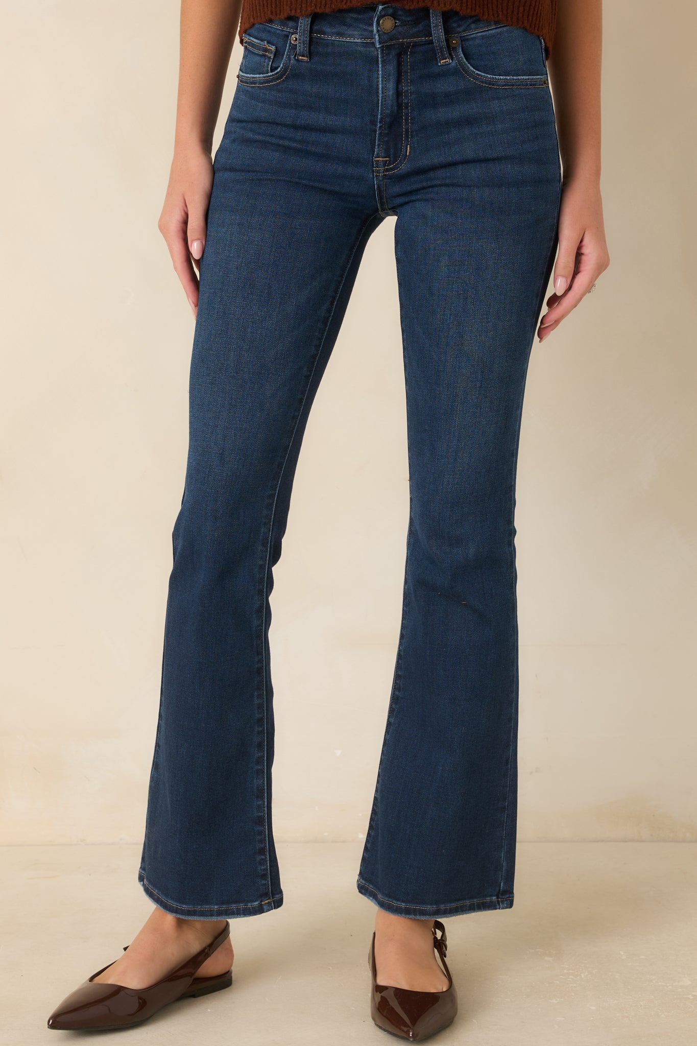 Close view of the mid-rise waistband with button-and-zip closure, contrast stitching, and classic five-pocket detailing on dark wash denim.