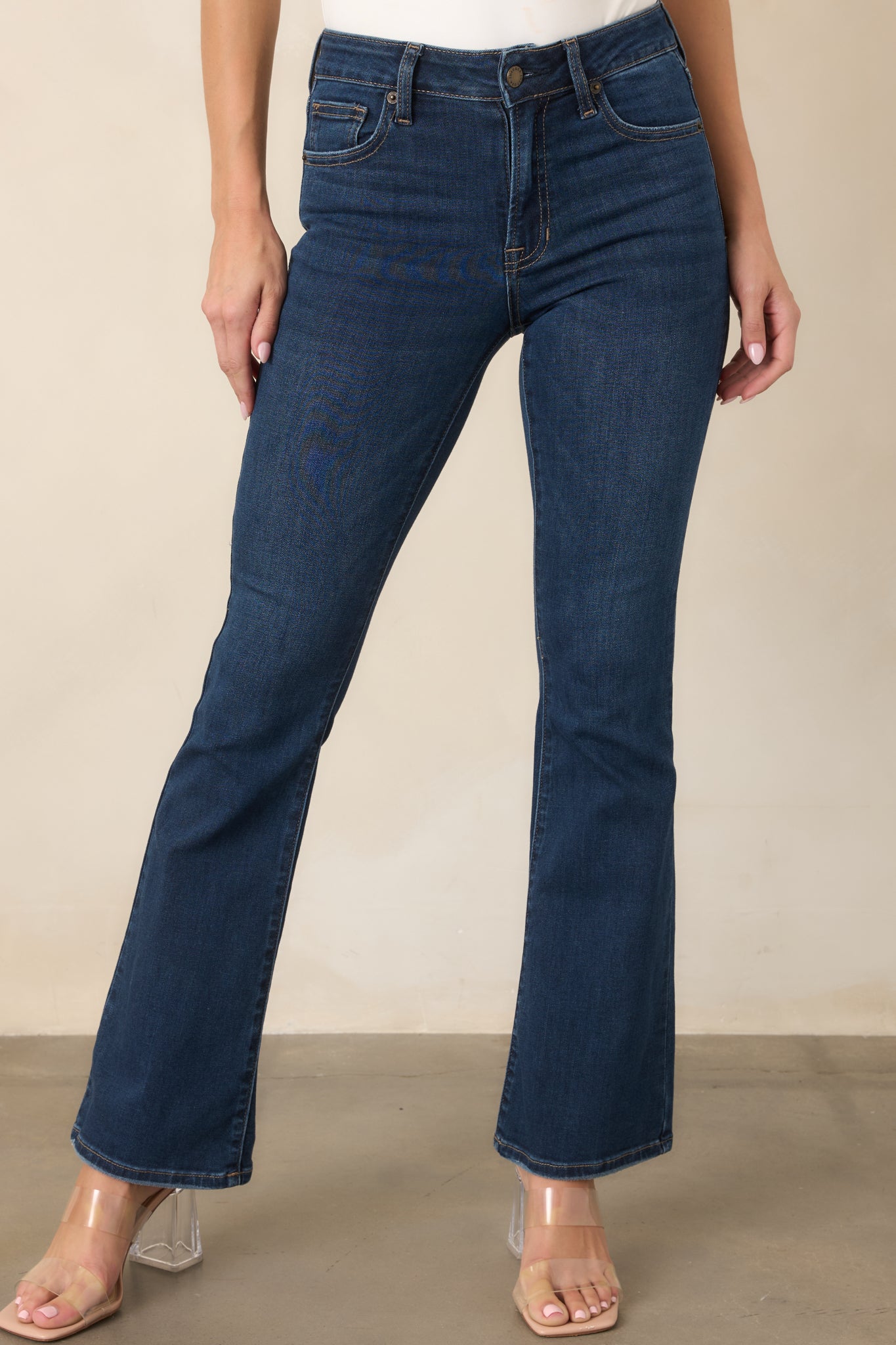 Dark-wash jeans highlighting the mid-rise waistband, belt loops, button closure, and contrasting topstitching.