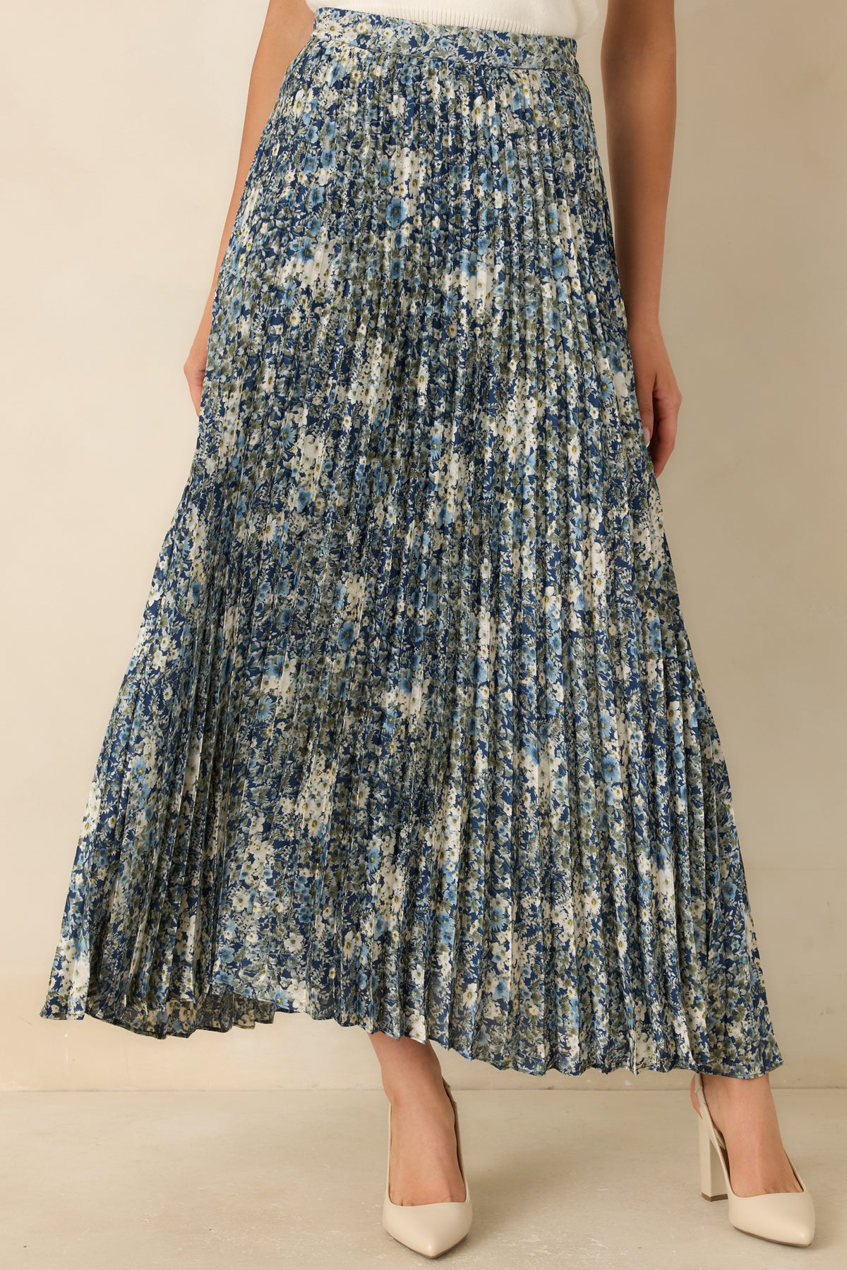 Fine accordion pleats create texture across the deep blue skirt with its delicate floral print.