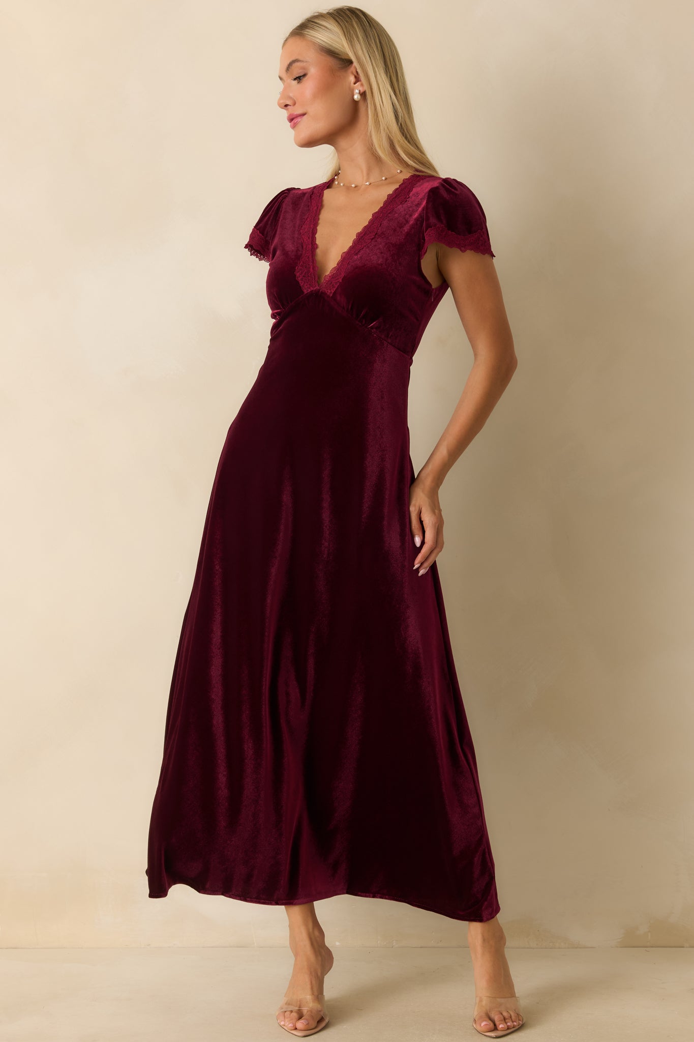 Maxi dress in deep cranberry red velvet highlighting short flutter sleeves and delicate lace along the V-neckline.