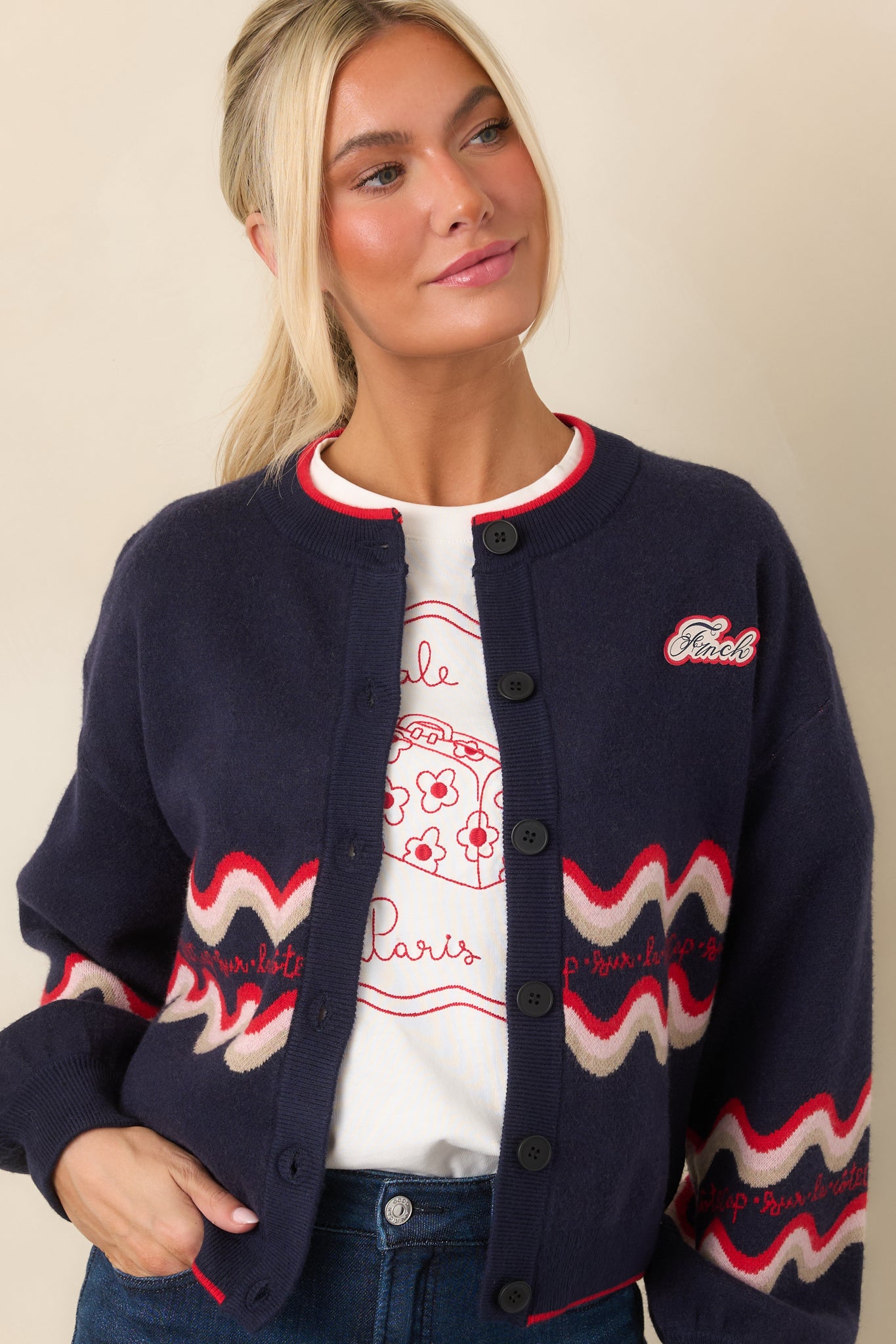 Deep navy knit cardigan with colorful wave detailing across the front, red contrast trim, long sleeves, and a relaxed layering silhouette.