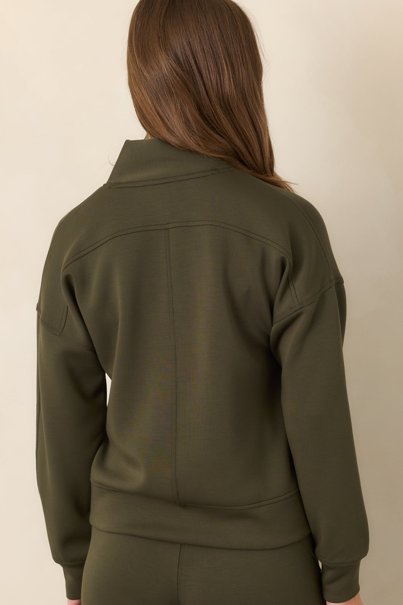 Rear view of the deep olive top showcasing the dropped shoulders, relaxed silhouette, long sleeves, and banded cuffs.