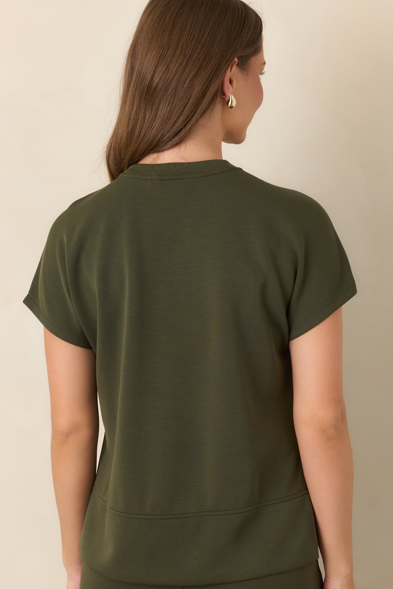 Rear view of the deep olive top showcasing its smooth fabric, short sleeves, elongated high-low hem, and side slits.