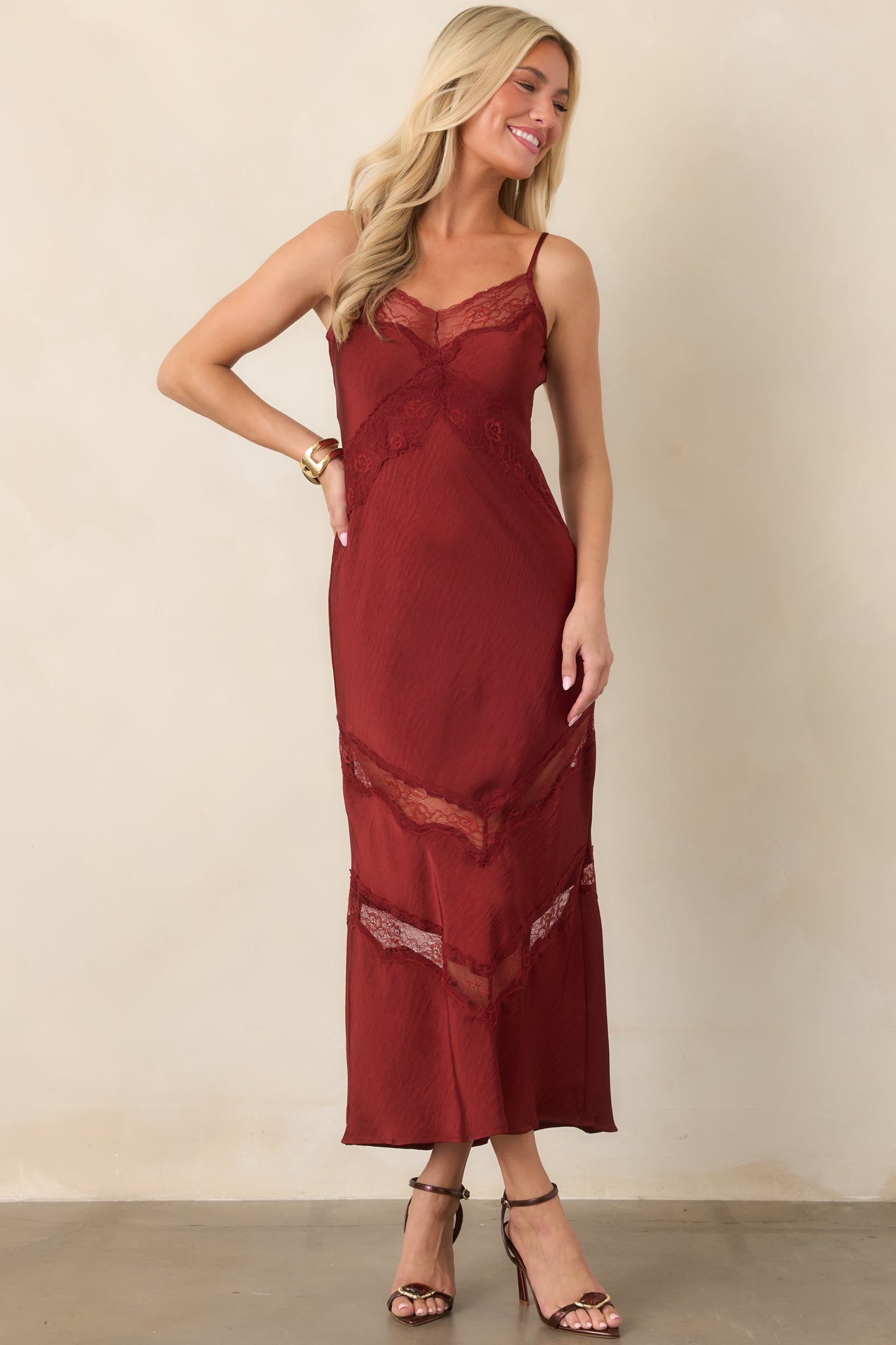 Deep red satin slip dress with a V-neckline, adjustable spaghetti straps, and decorative lace panels through the skirt