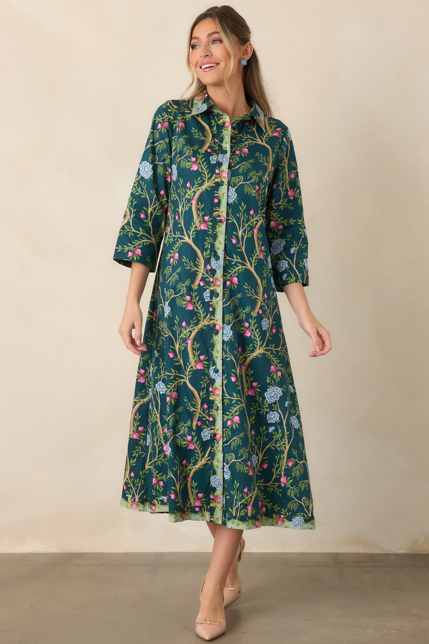 Deep teal botanical cotton dress with a vibrant mix of tan branches, green leaves, pink buds, and blue blooms, finished with three-quarter sleeves and a flowing skirt.
