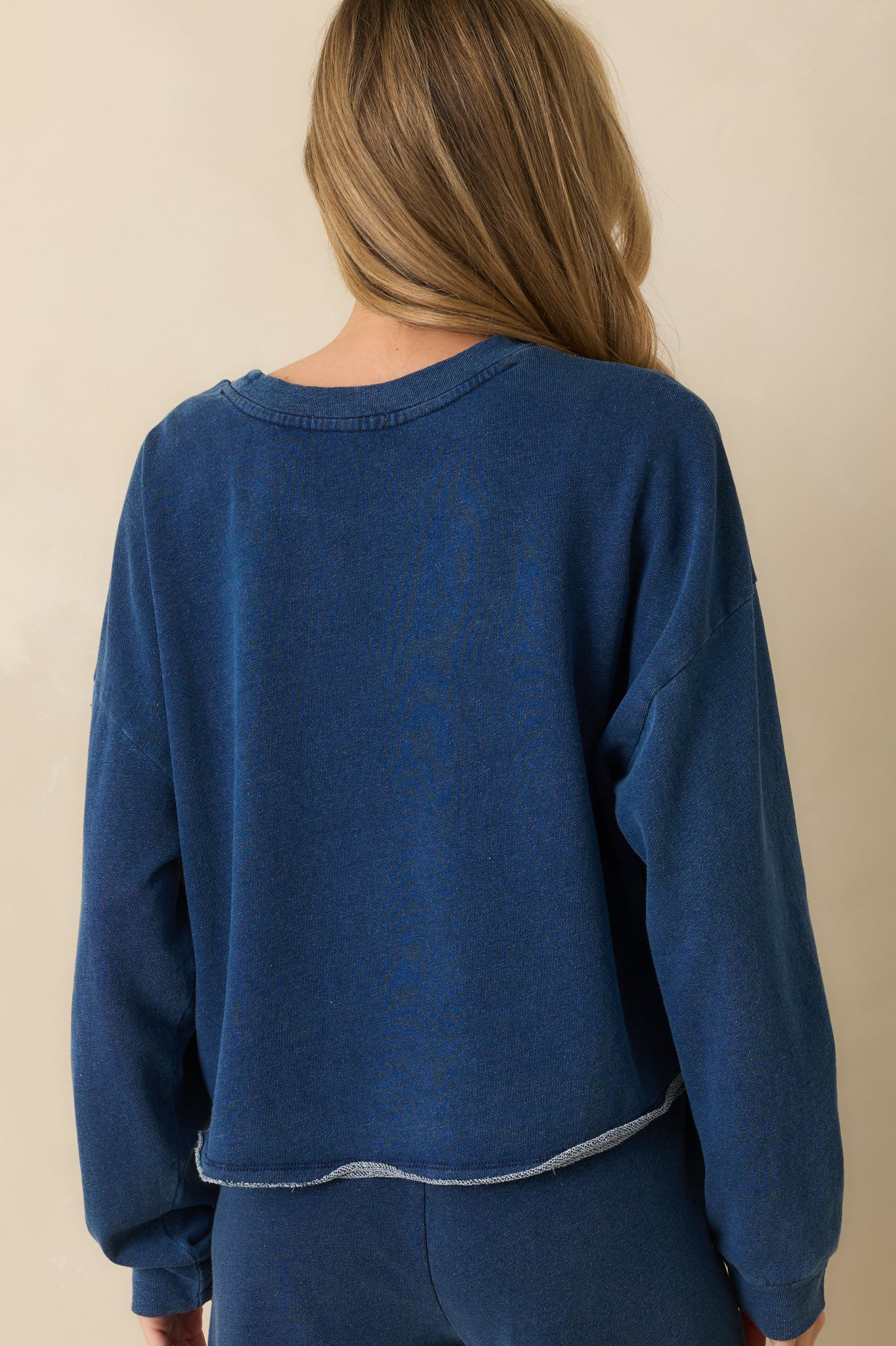 Rear view of the denim blue sweatshirt displaying the smooth back and long sleeves.