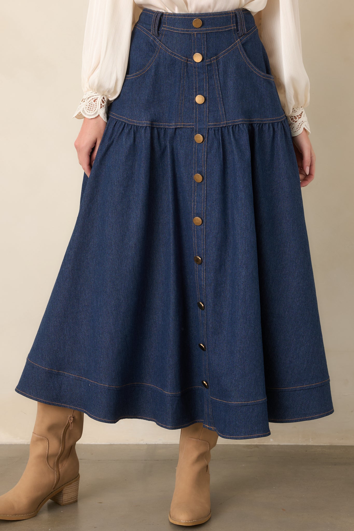 Denim maxi skirt with prominent gold-tone buttons, contrast stitching, front pockets, and a softly widening silhouette.
