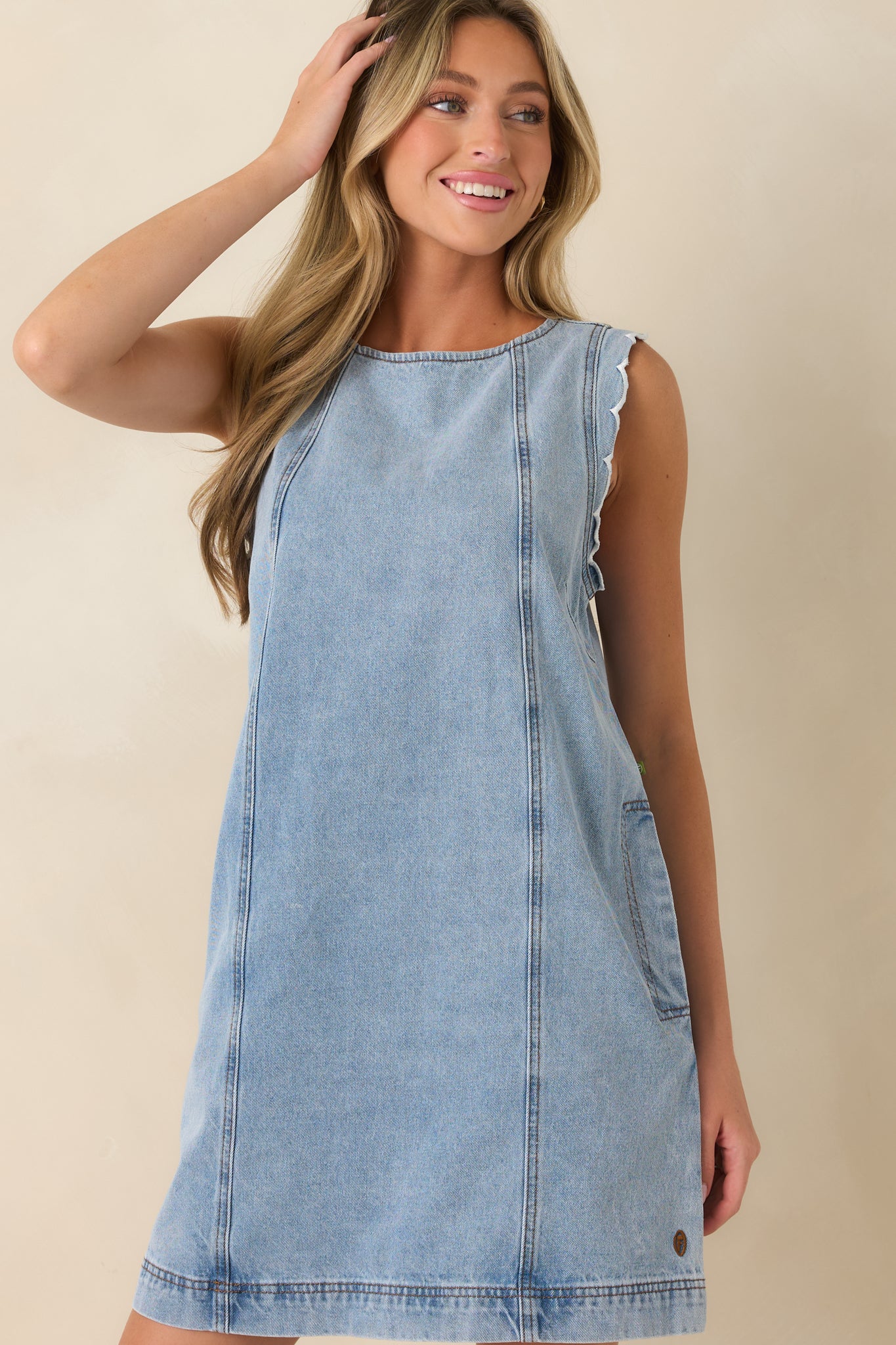 Detailed view of the denim mini dress highlighting the scalloped arm opening trim, soft vintage wash, and structured vertical seam detailing.