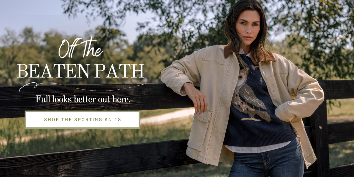 Model wearing a navy owl knit sweater with a tan jacket. Text reads: "Off The Beaten Path. Fall looks better out here."