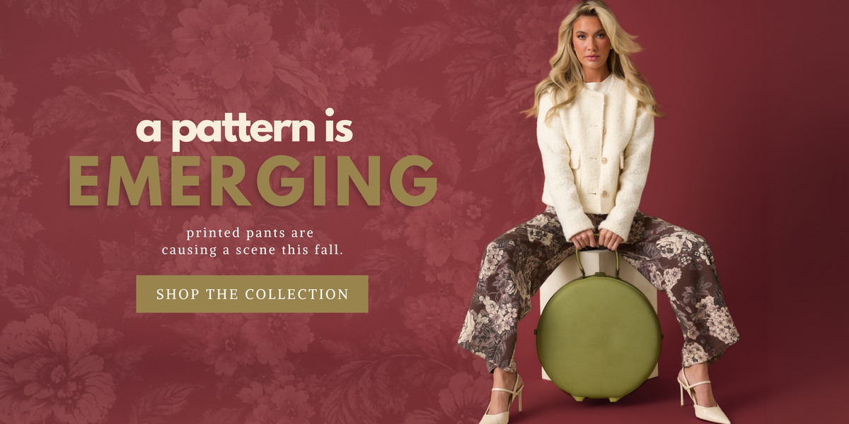 Model wearing a white jacket and floral pants, against a burgundy floral backdrop. Text reads: "A pattern is emerging. Printed pants are causing a scene this fall. Shop the collection."