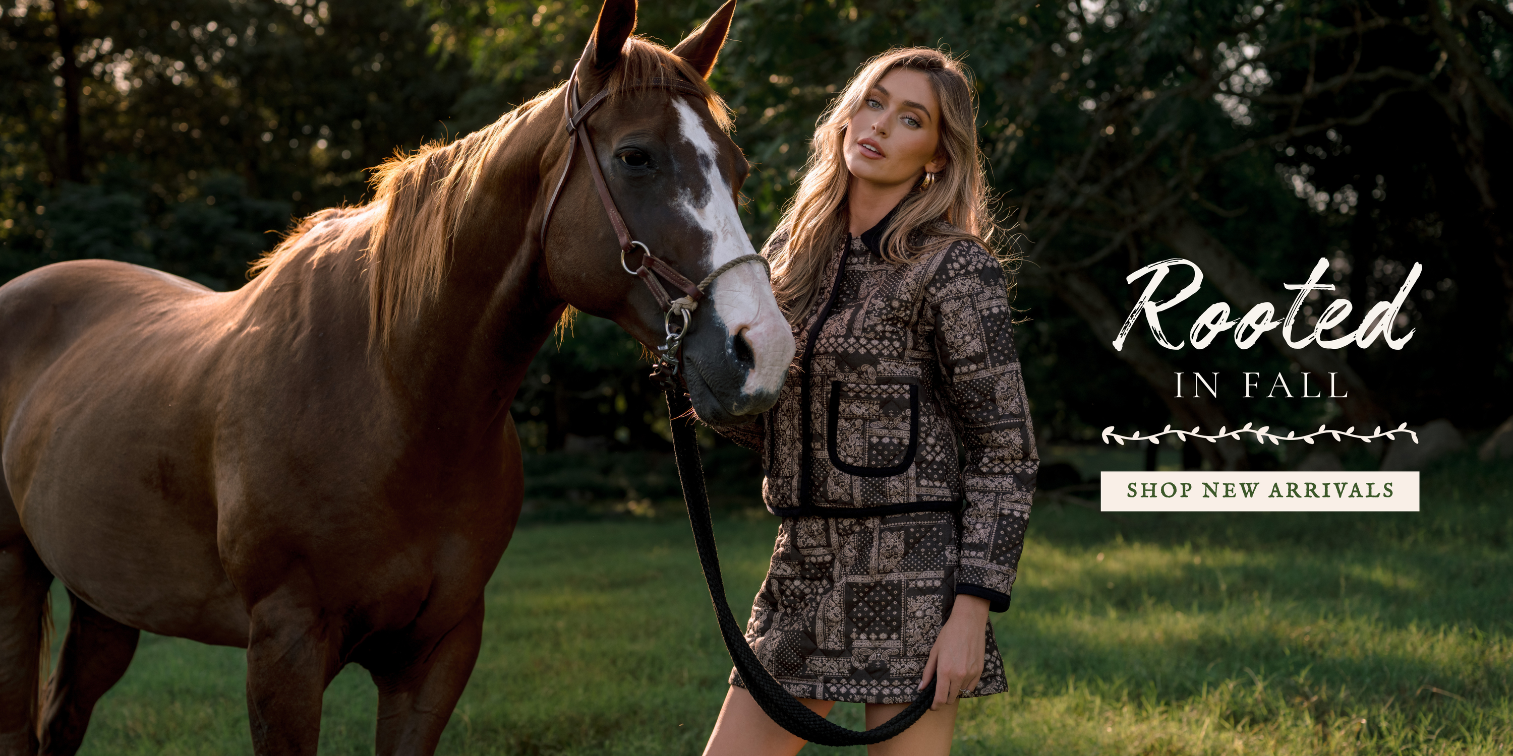 Model wearing a patterned jacket and shorts stands beside a horse in a wooded field, with text reading “Rooted in Fall” and “Shop New Arrivals.”