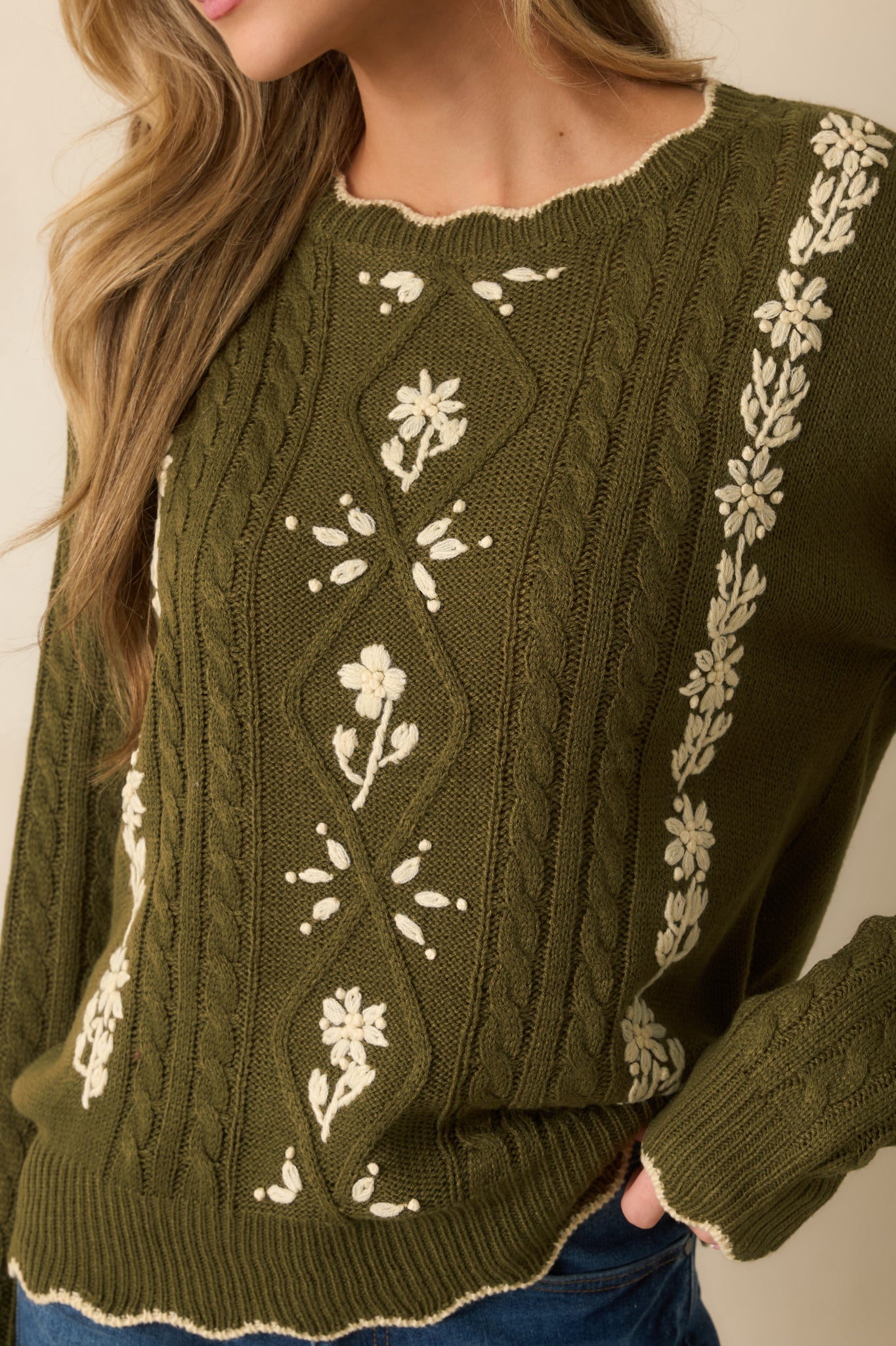Detailed view of ivory floral embroidery against the textured olive cable knit fabric.