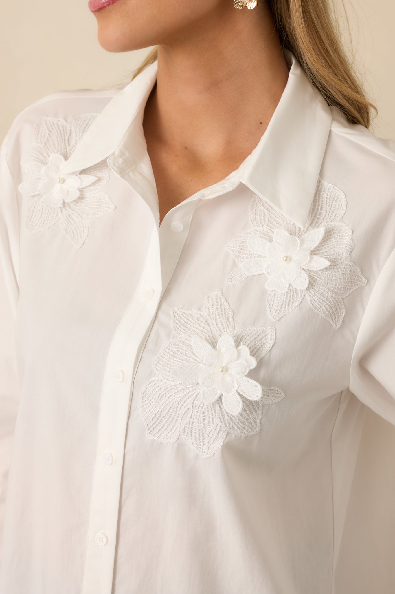  Detailed close-up of floral appliqué on white woven blouse, showing stitching and texture of front fabric.