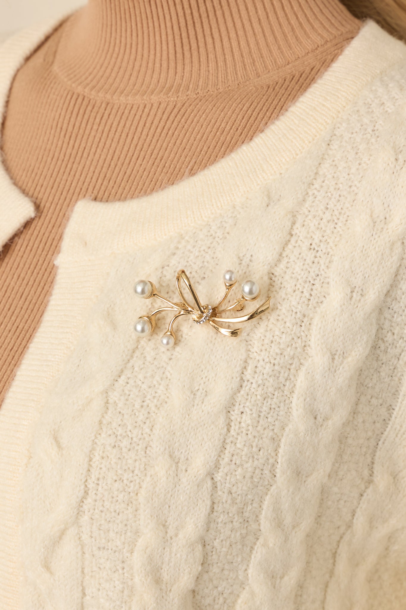 Close-up detail of the bow-inspired pearl brooch showing gold-tone metalwork and faux pearl embellishments.