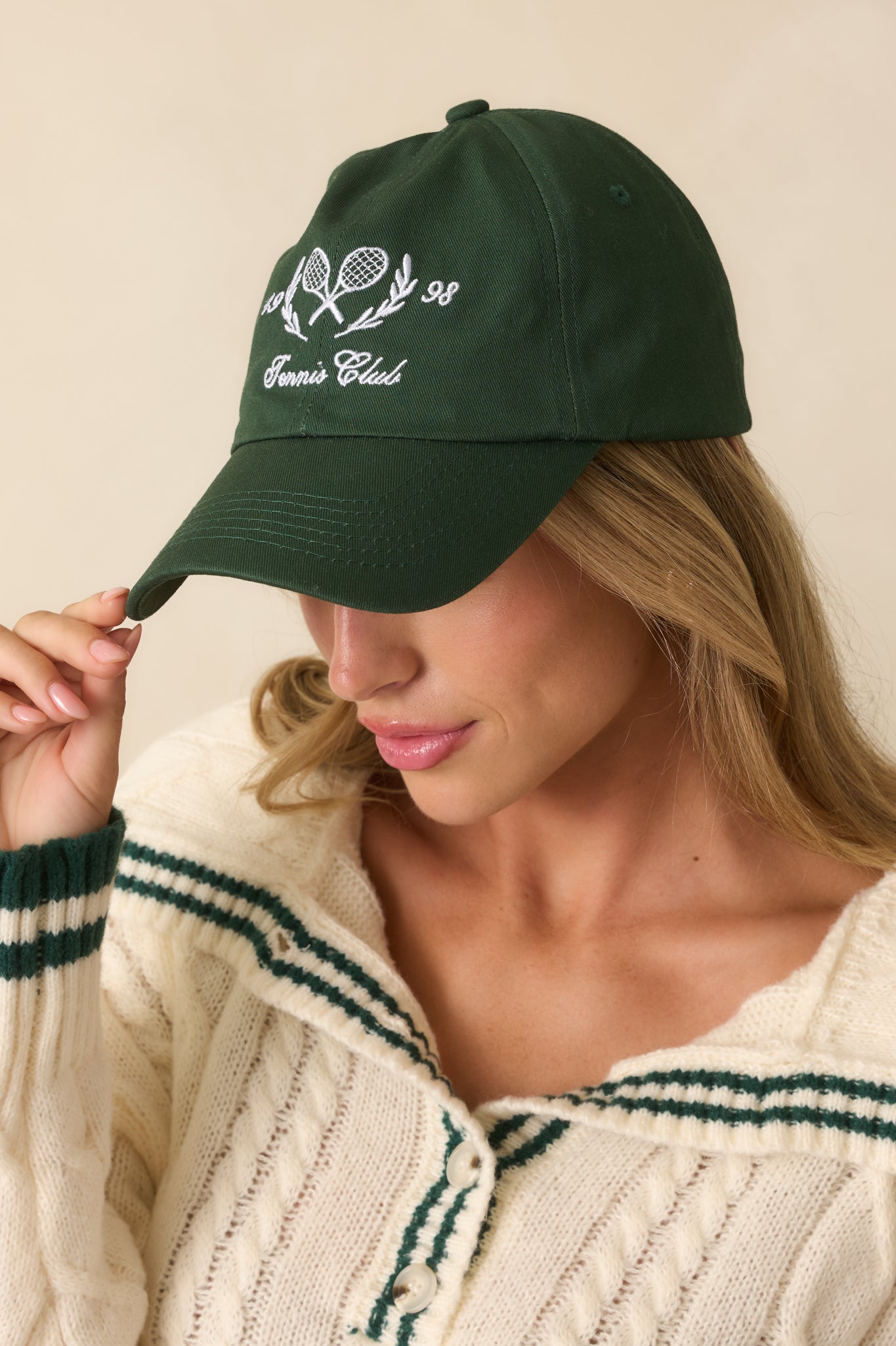 Detail of the curved brim, stitched eyelets, and top button of the green baseball cap.