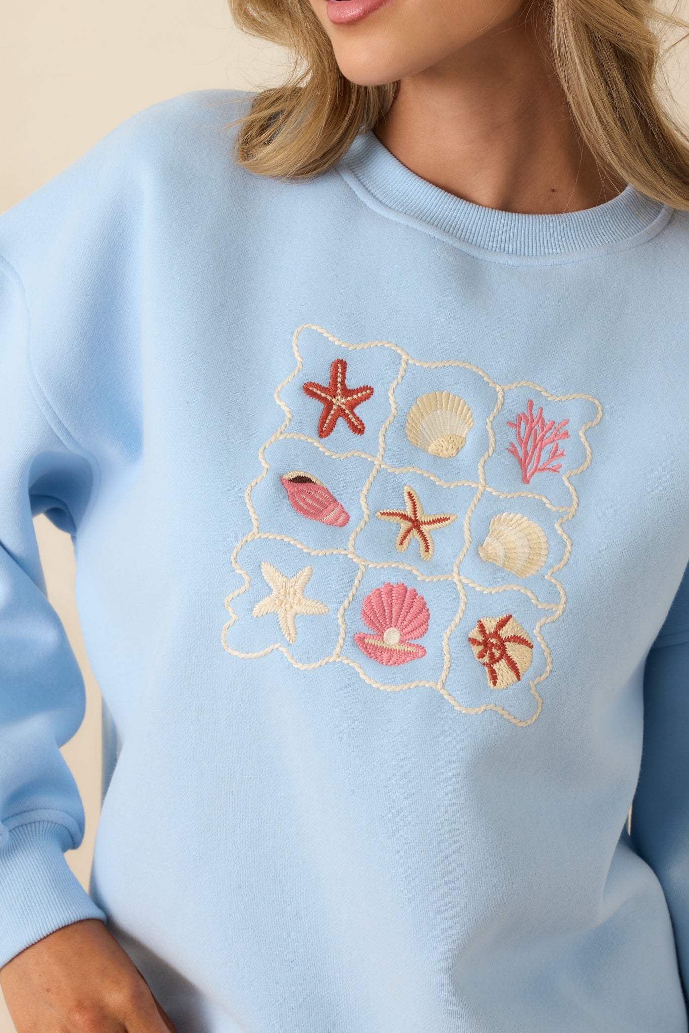 Close detail of the embroidered patch stitching on the soft light blue sweatshirt fabric.