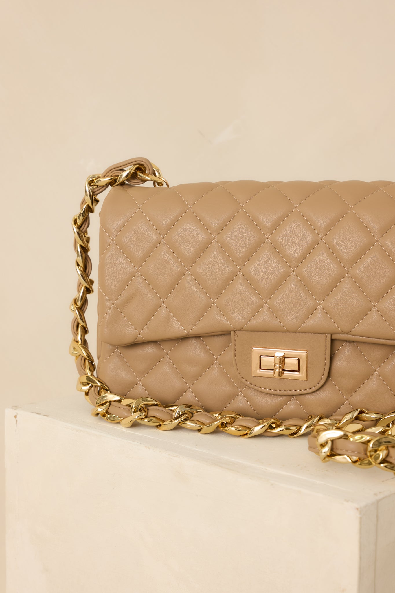 Close-up of tan quilted handbag showcasing turn-lock closure, chain strap, and gold hardware