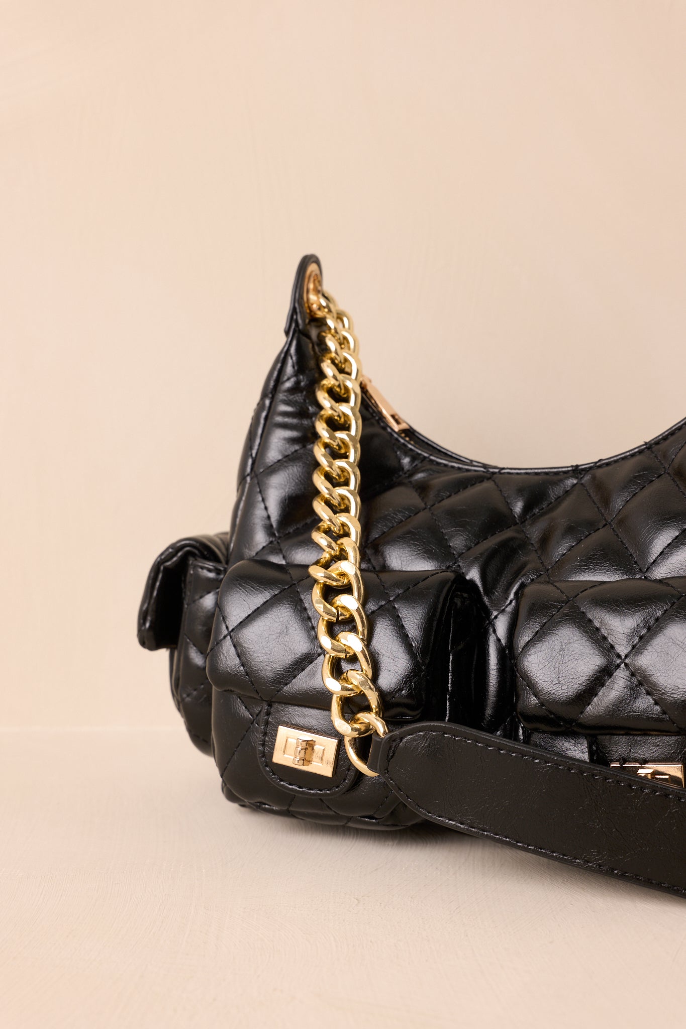 A close-up detail of the black handbag highlighting the quilted stitching, gold turn-lock closure, and polished hardware.