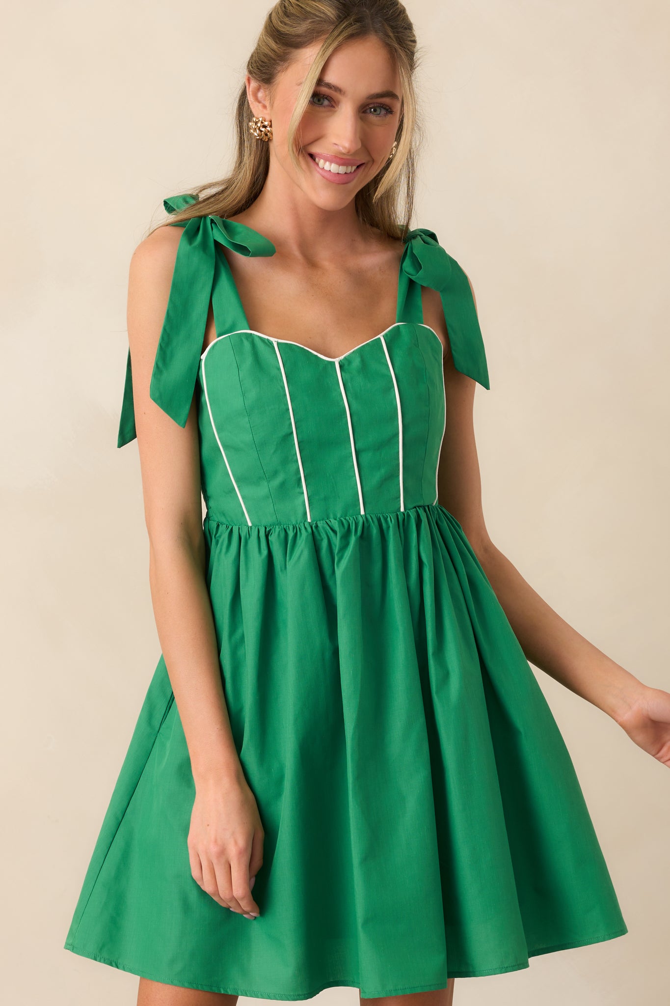 Detail of the mini dress’s white piping along the green fabric, emphasizing the corset-style structure.