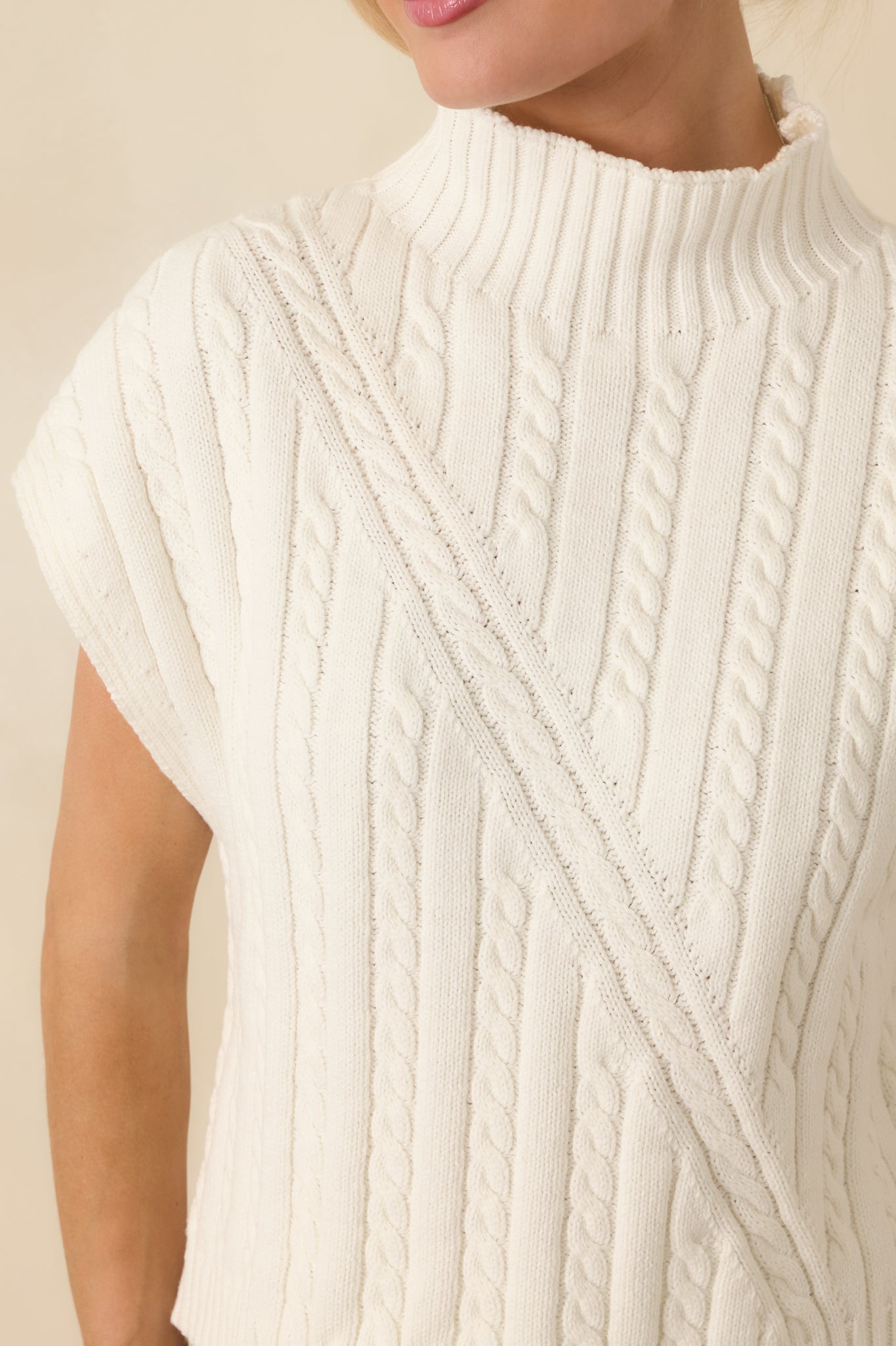 Close-up detail of the ivory cable knit sweater showcasing the intricate cable pattern and ribbed trim.