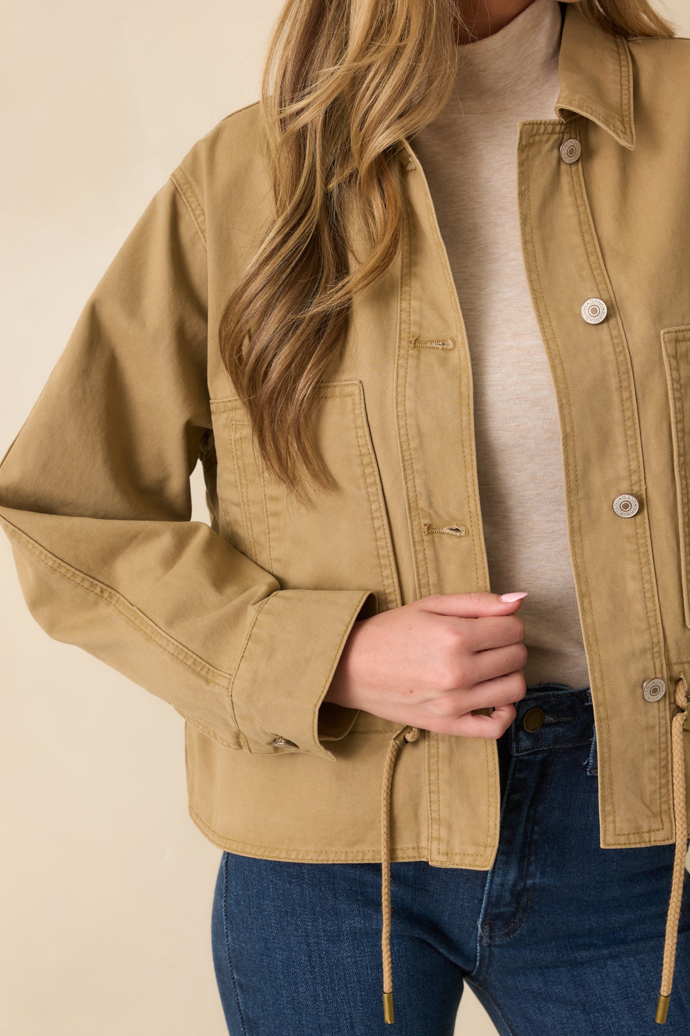 Detail view of the tan utility jacket showing the woven fabric, buttons, and pocket seams.