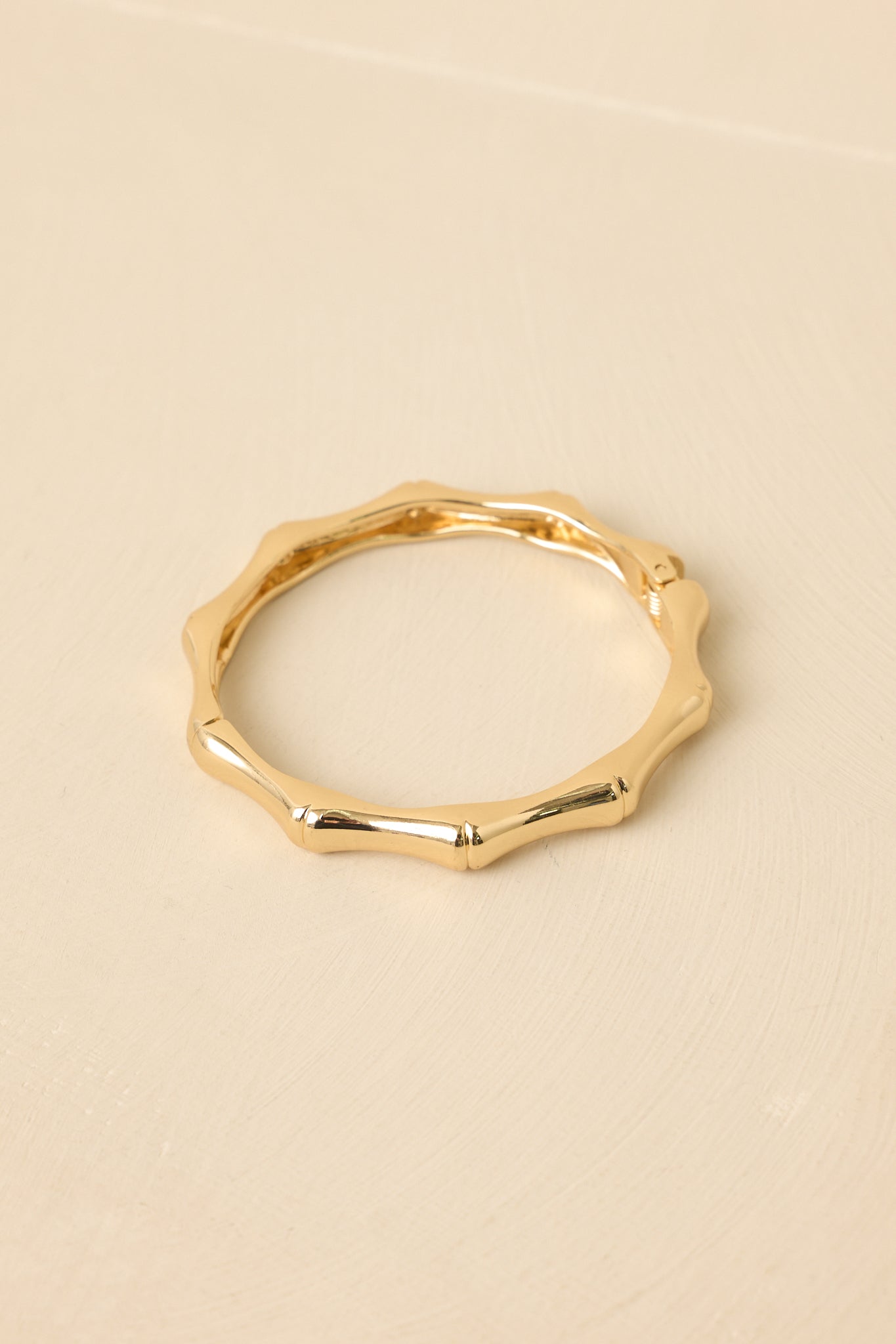 Detailed close-up of the gold-tone bracelet emphasizing the bamboo-like texture, hinge mechanism, and secure snap clasp.