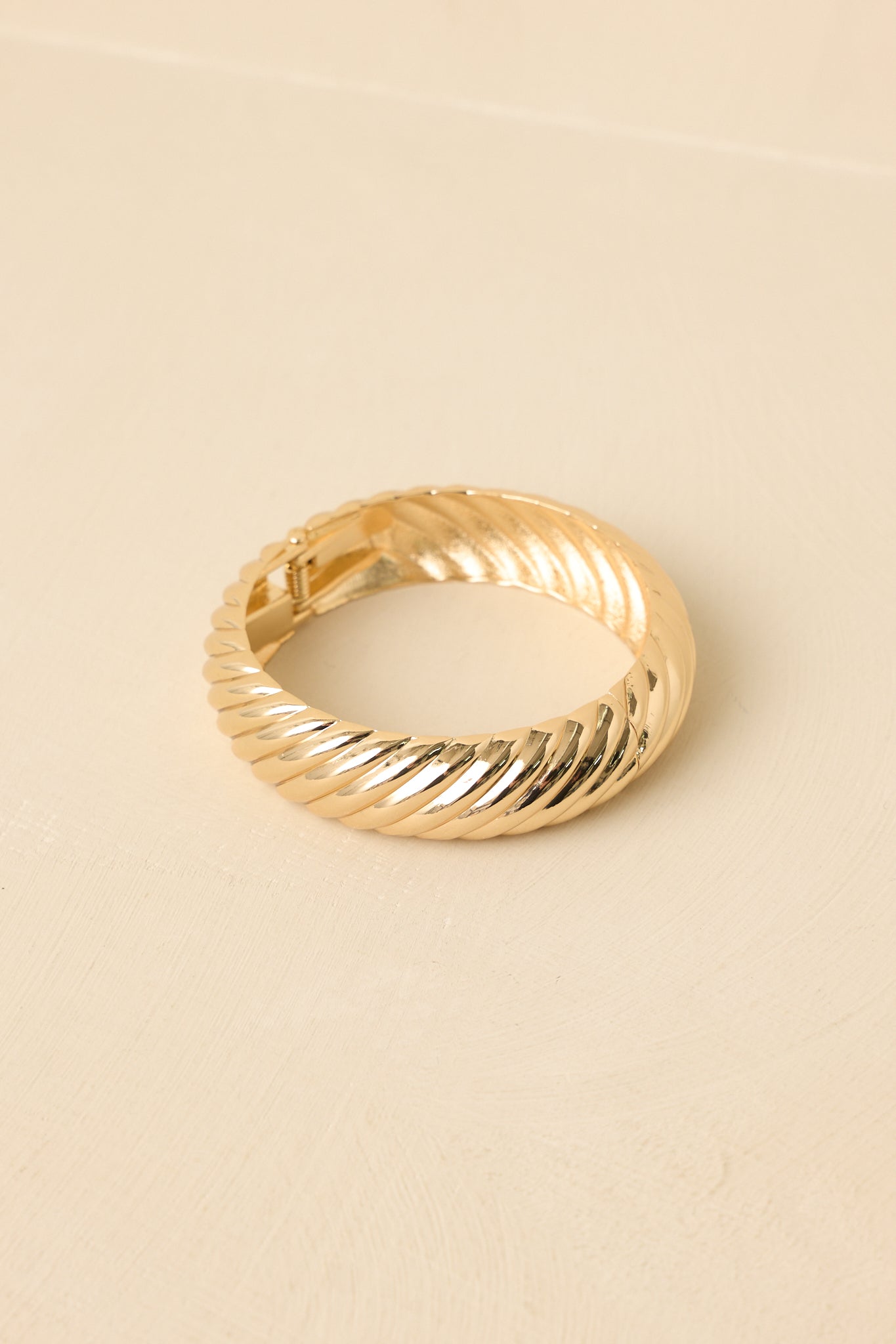 Detailed close-up of the gold-tone bracelet showcasing the twisted texture, hinge mechanism, and snap clasp closure.