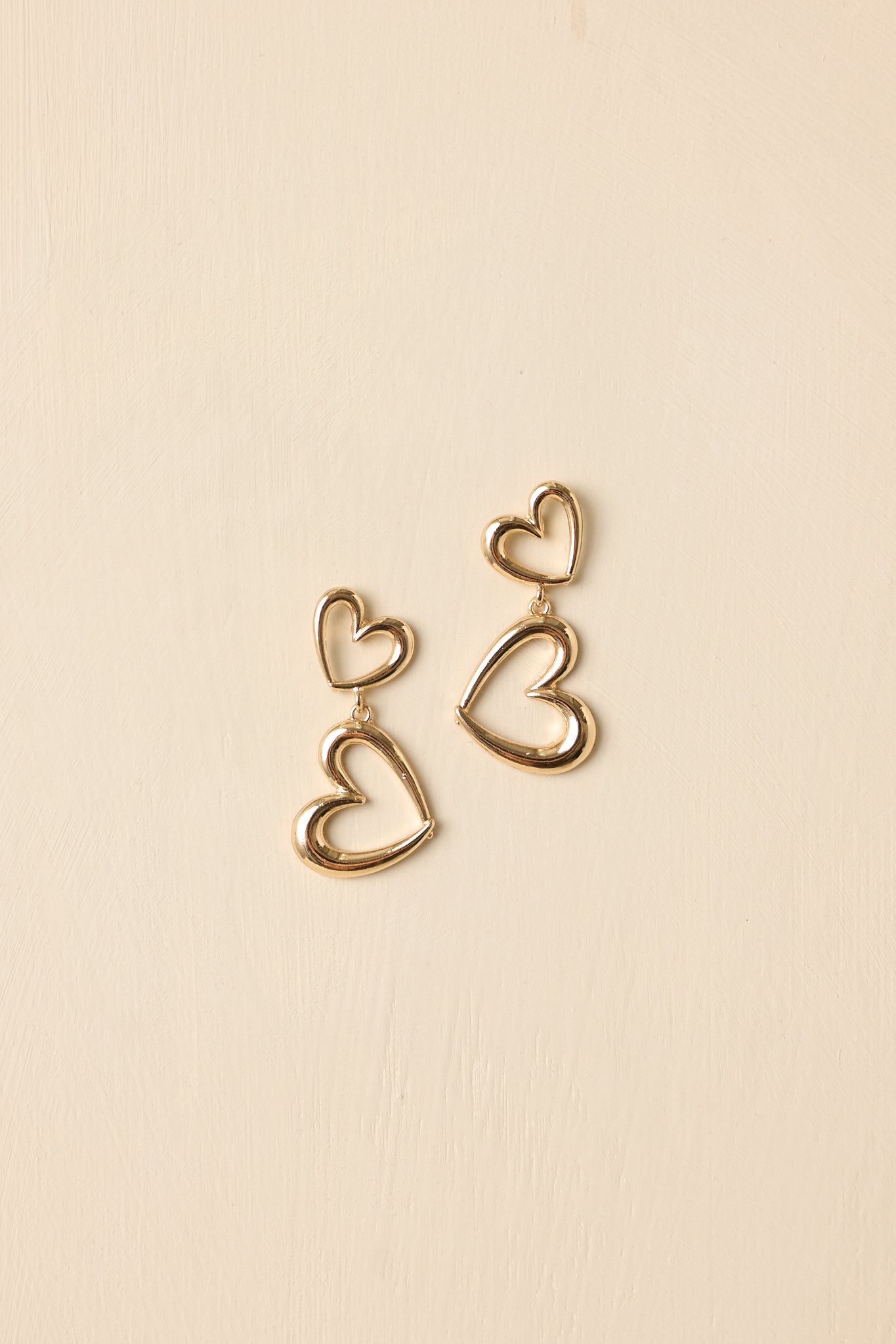 Detailed close-up of the gold-tone drop earrings focusing on the double open-heart design and reflective polished finish.