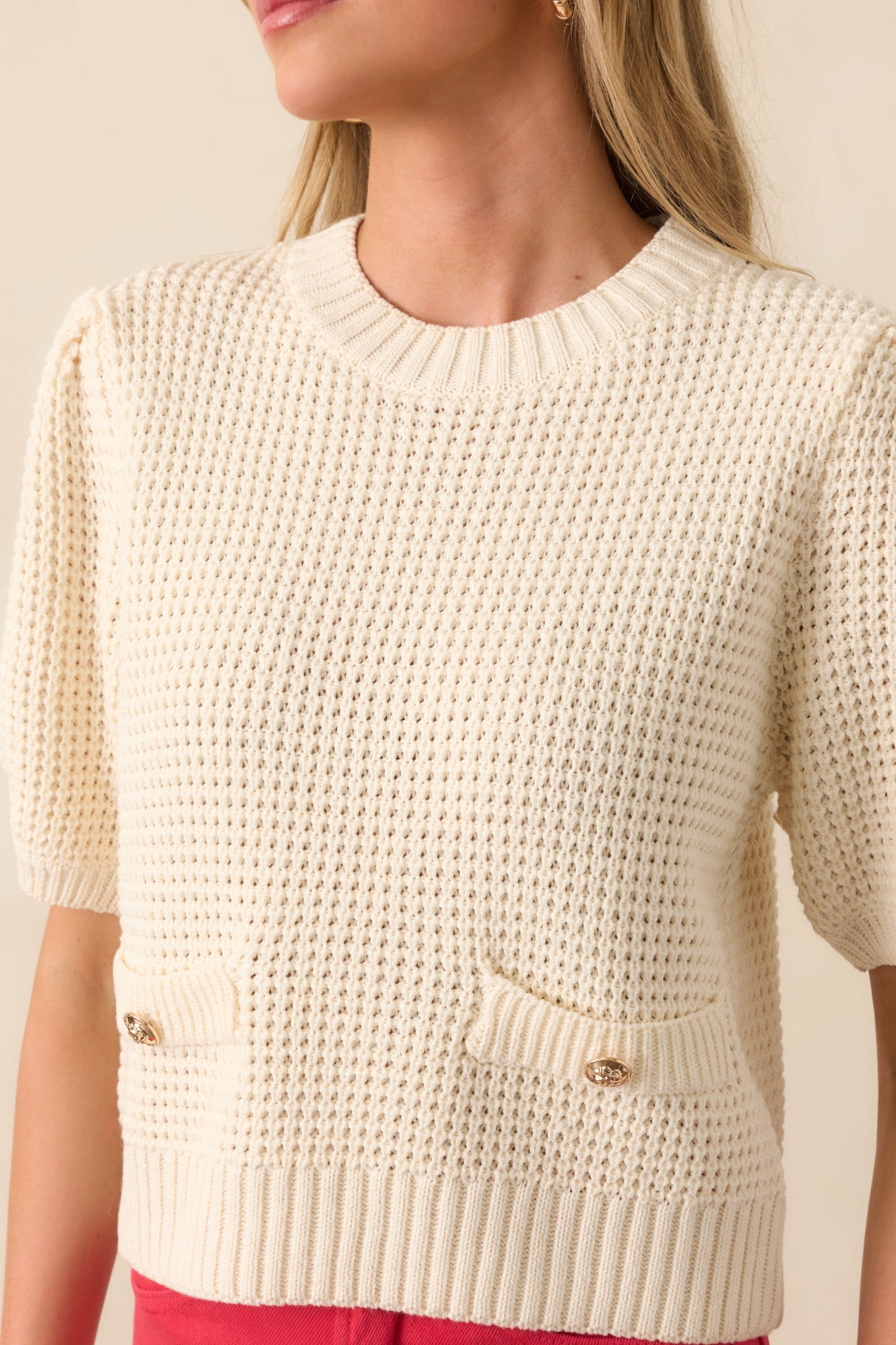 Detailed close-up of the faux pocket and gold decorative buttons against the ivory knit fabric.