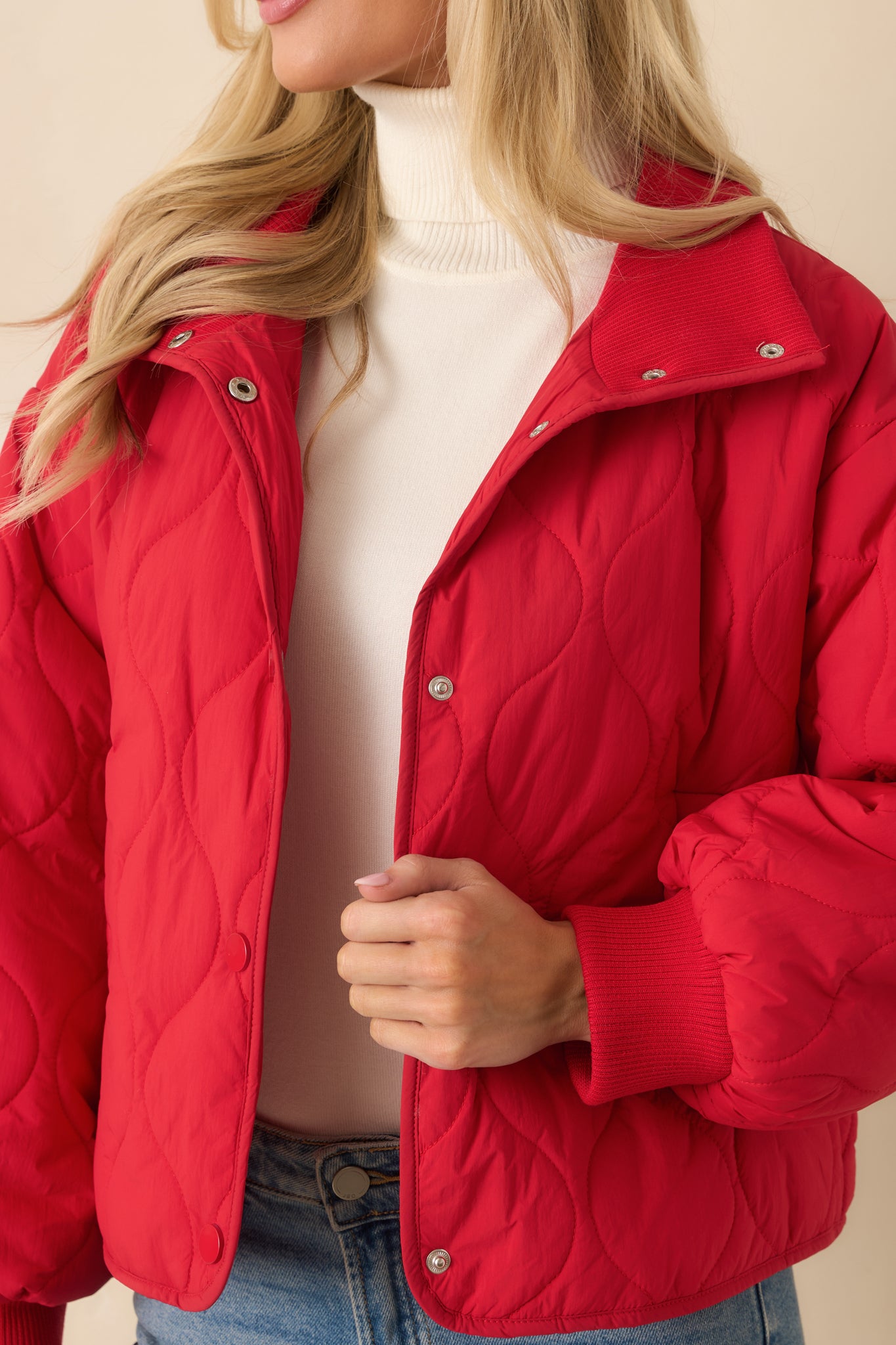 Detailed close-up of the red quilted jacket’s snap-front hardware and textured stitching.