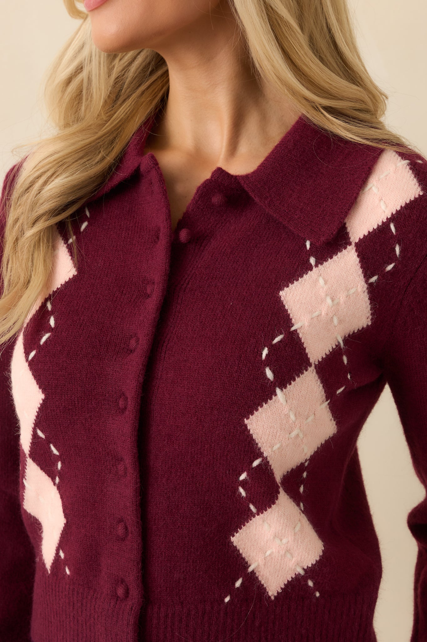 Detailed close-up of tonal buttons, blush pink argyle pattern, and textured knit fabric.